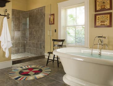 A stylish bathroom featuring a freestanding bathtub, a glass shower, a decorative rug, and natural light from a window.