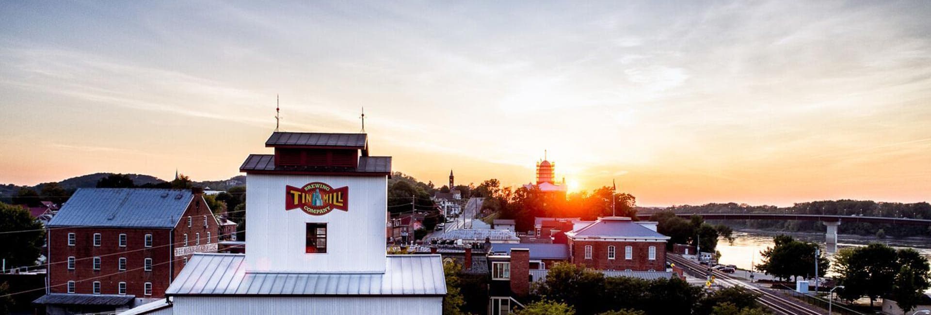 A scenic view of the Tin Mill Brewing Company at sunset, surrounded by buildings and hills.