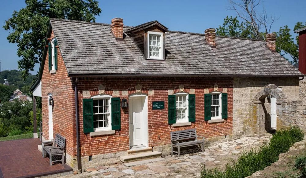 Historic brick house with green shuttered windows and a stone archway, set against a clear blue sky.