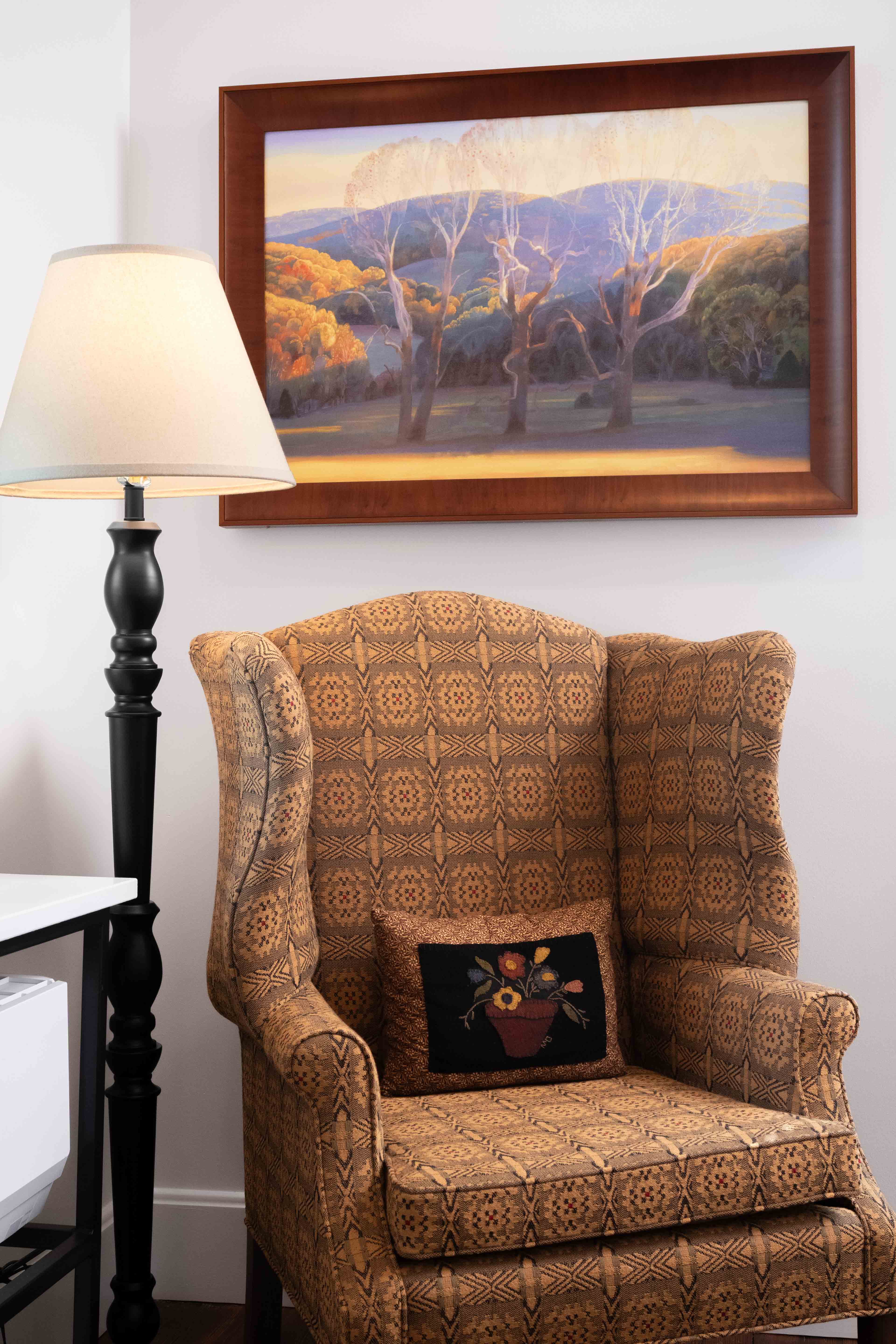 A patterned armchair next to a black lamp, with a nature painting hanging above.