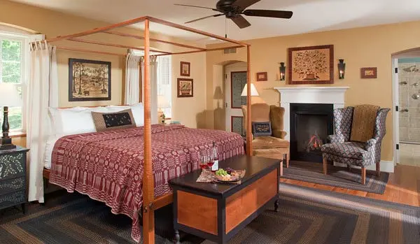 A cozy bedroom featuring a four-poster bed, a fireplace, and a comfortable armchair.