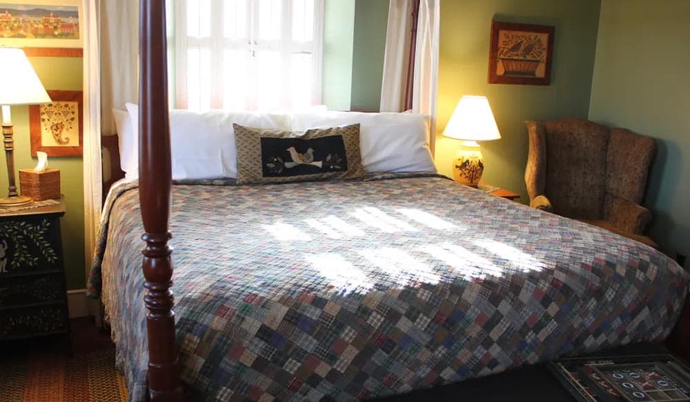 Cozy bedroom featuring a large quilted bed, decorative lamp, and comfortable armchair.