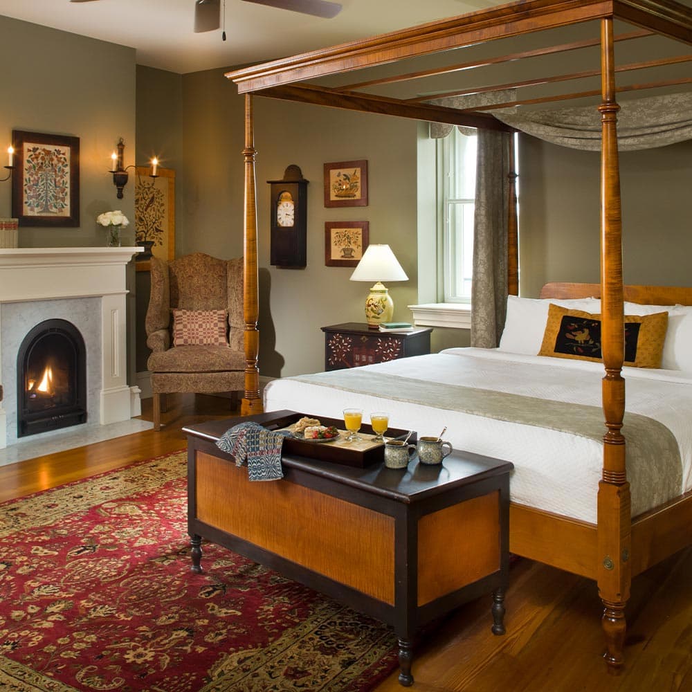 A cozy bedroom featuring a four-poster bed, fireplace, and a tray with breakfast.