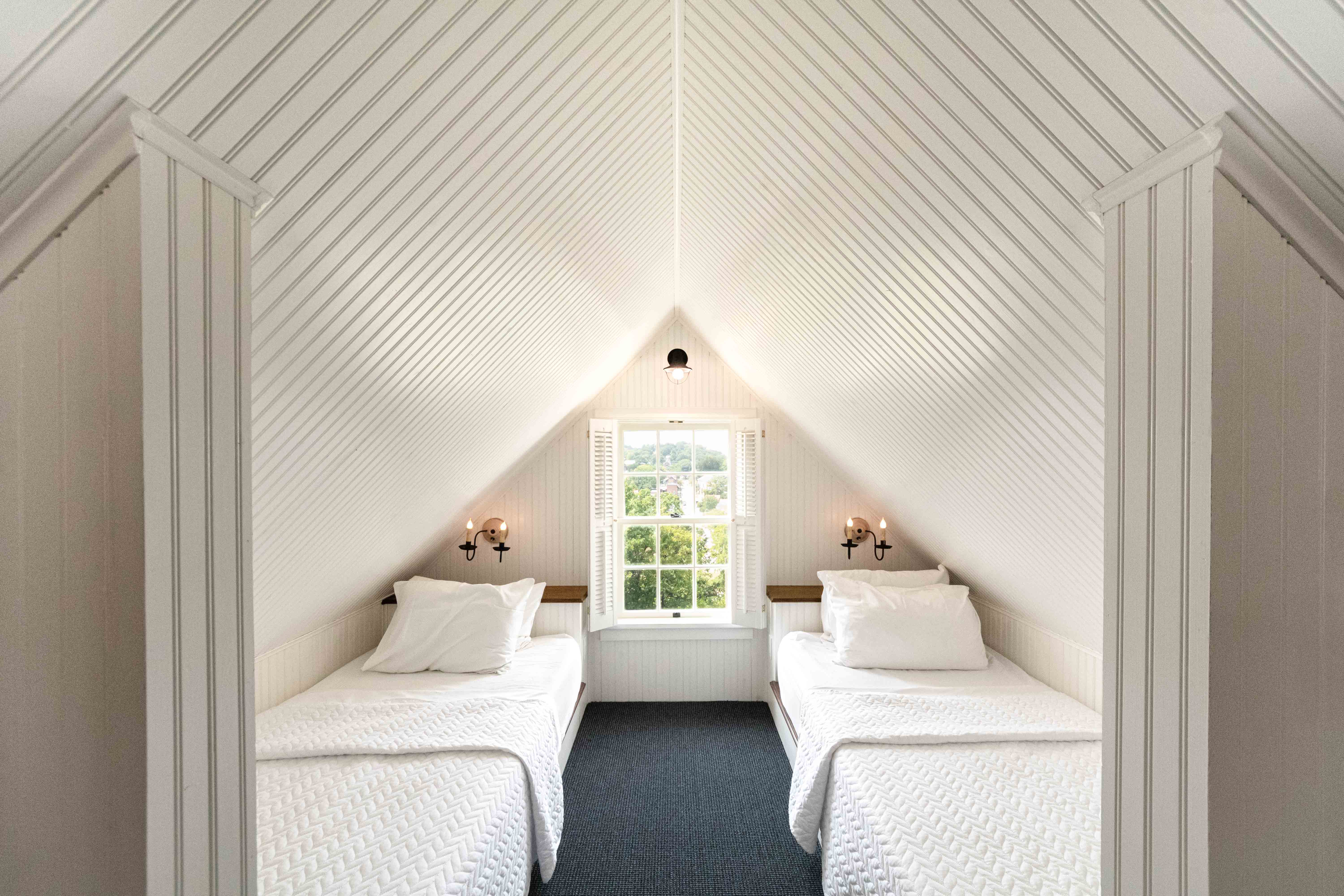 A bright, minimalist attic bedroom with two beds and a window overlooking greenery.