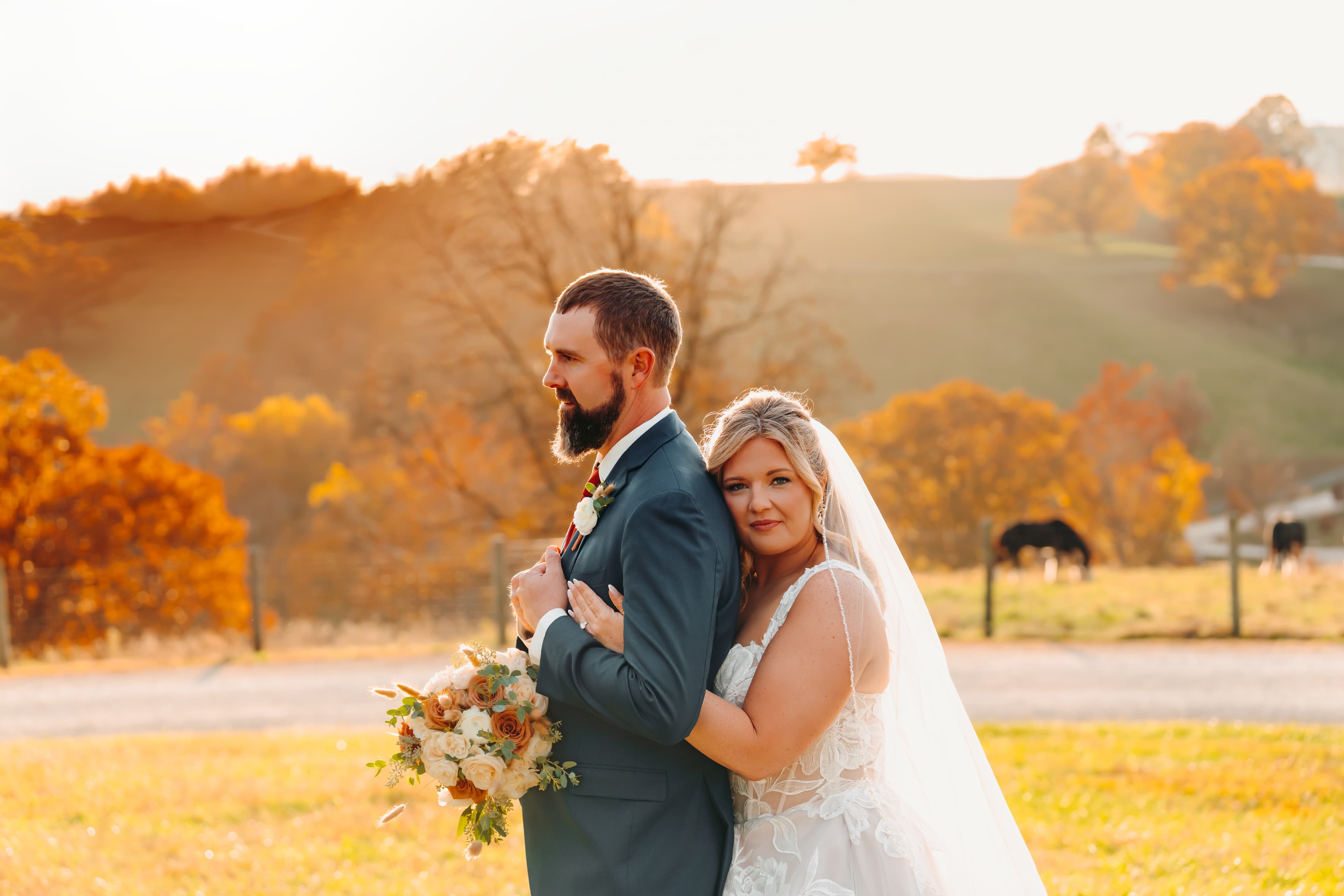A joyful couple stands together in a sunlit field, surrounded by autumn foliage.