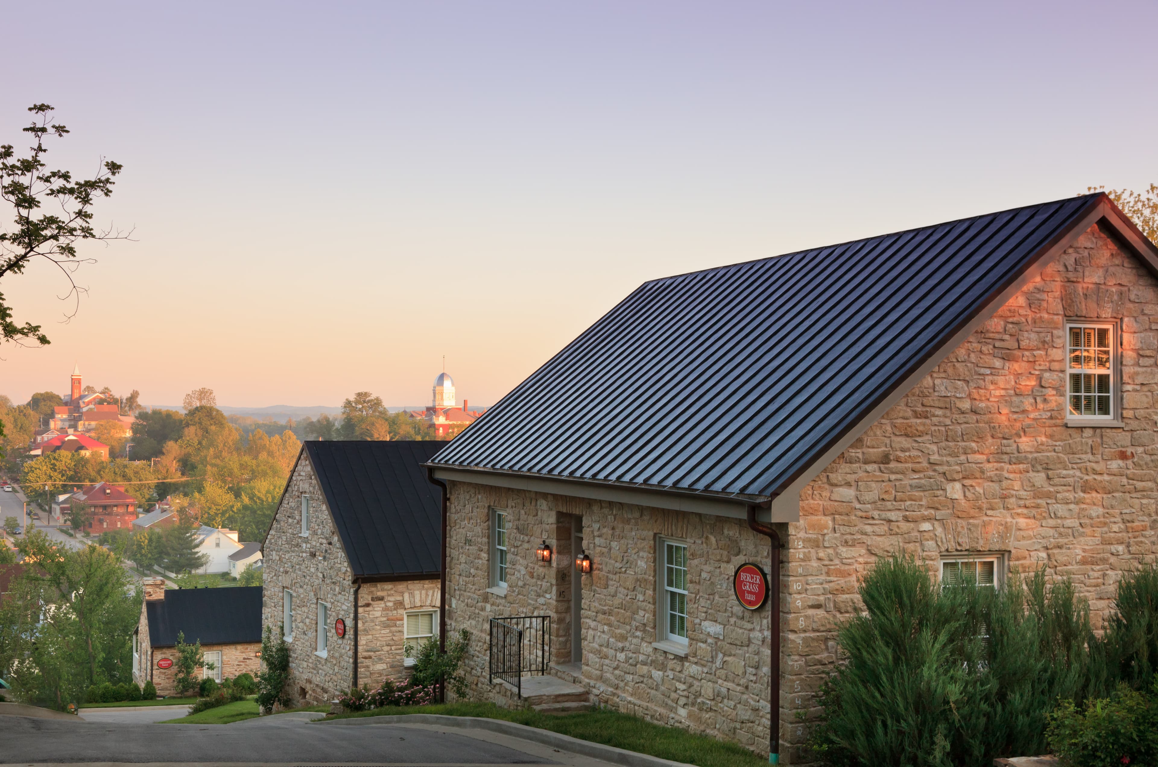 A picturesque view of stone houses on a hillside with a soft sunset glow and distant buildings.