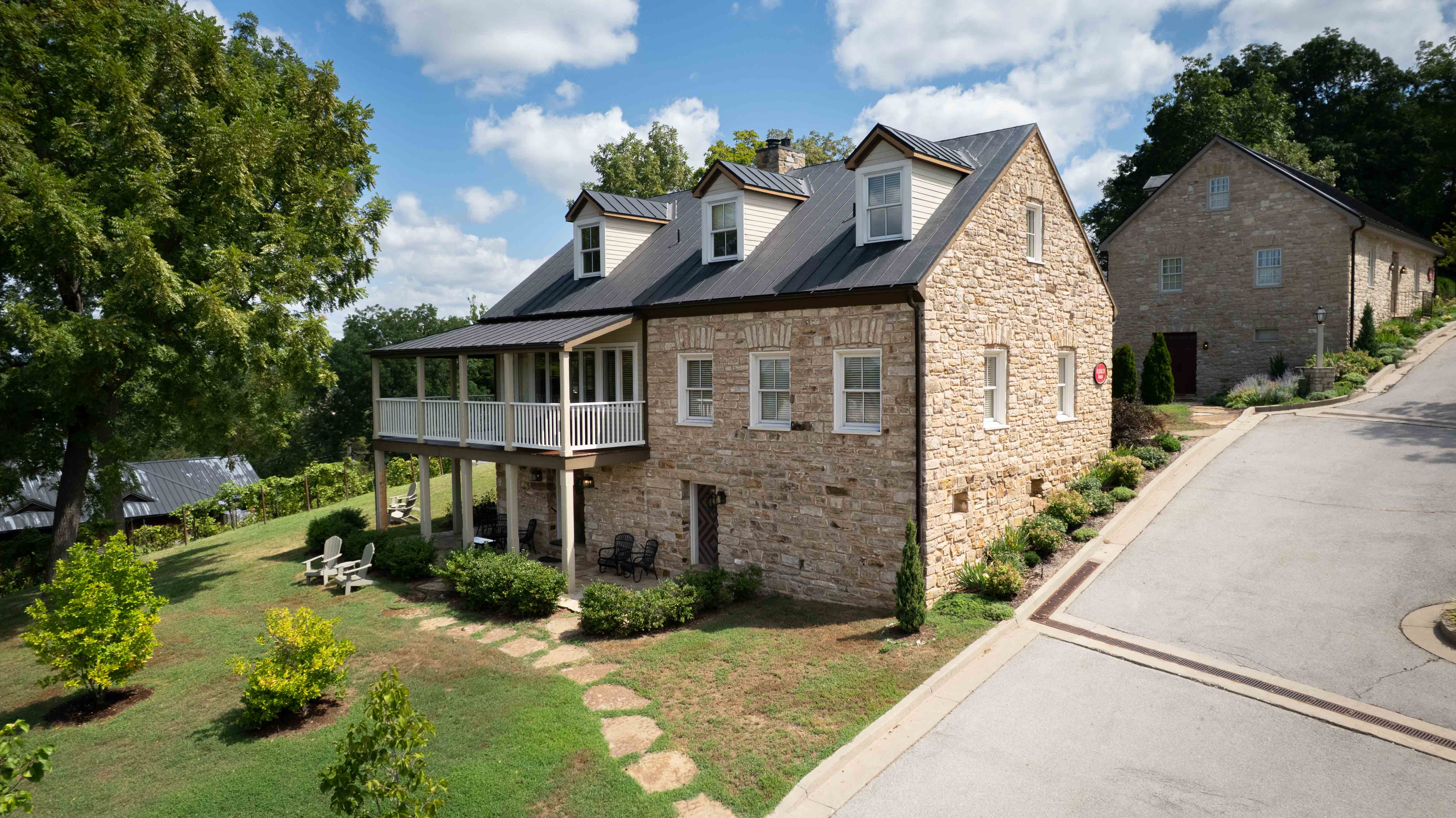 A stone house with multiple gables and a porch, surrounded by green grass and trees.