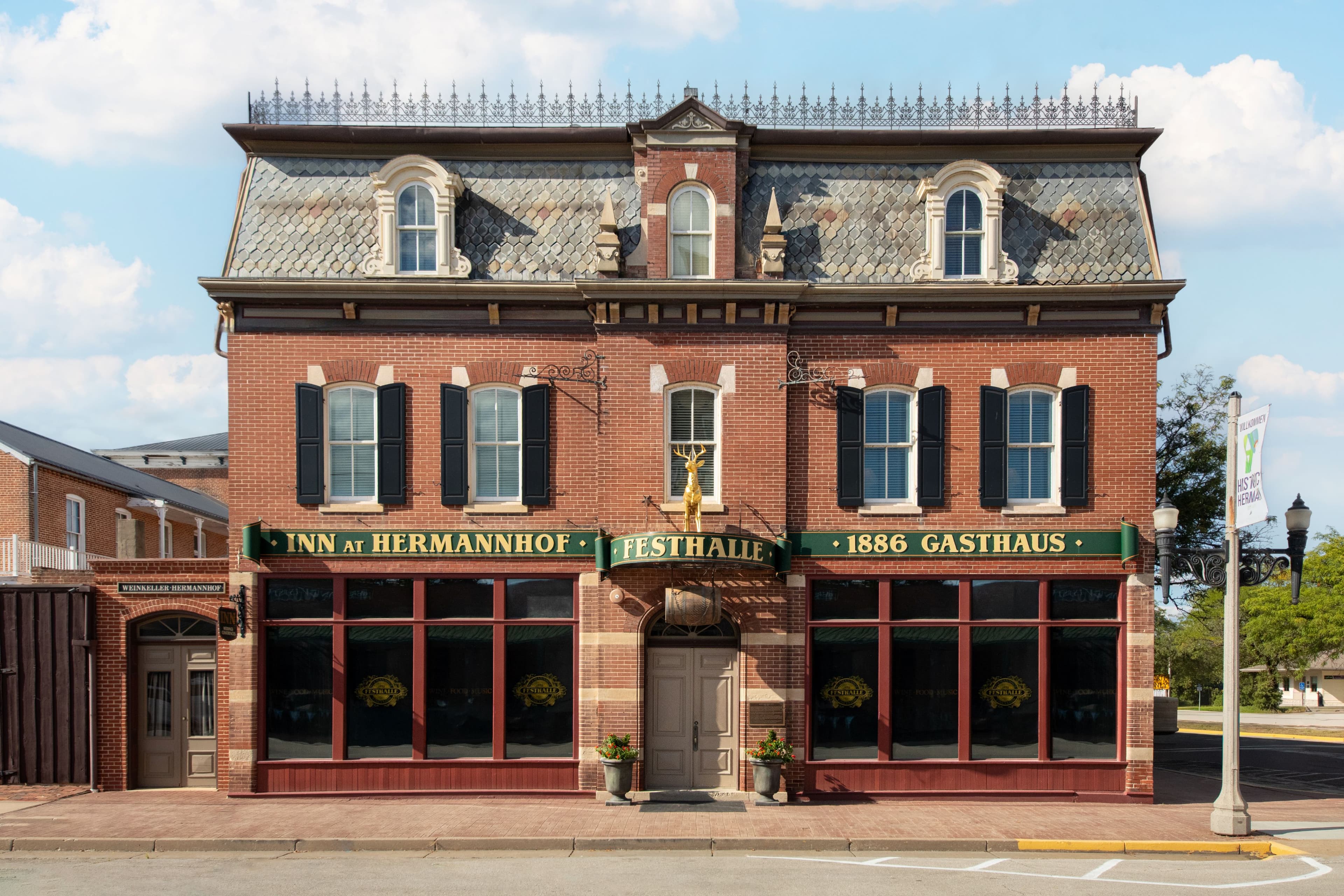 Historic brick building with green shutters and signage for "Inn at Hermannhof" and "1886 Gasthaus."
