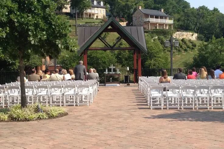 A gathering of guests seated in rows of white chairs at an outdoor wedding venue with a decorative arch.