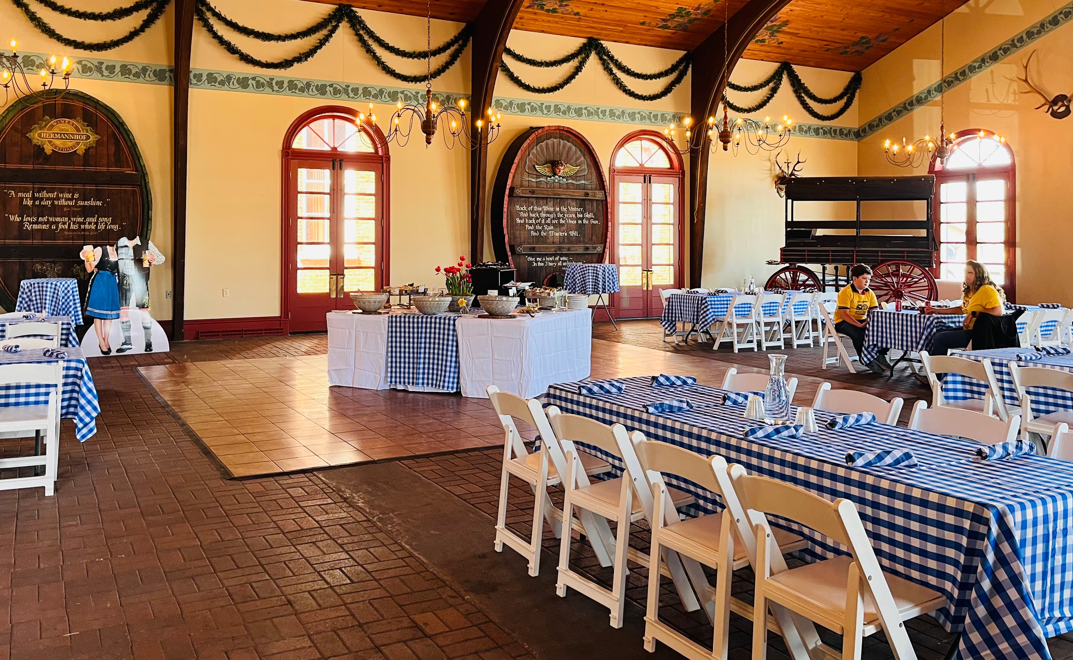 A spacious dining area featuring blue-and-white checkered tablecloths, decorated with flowers and rustic decor.