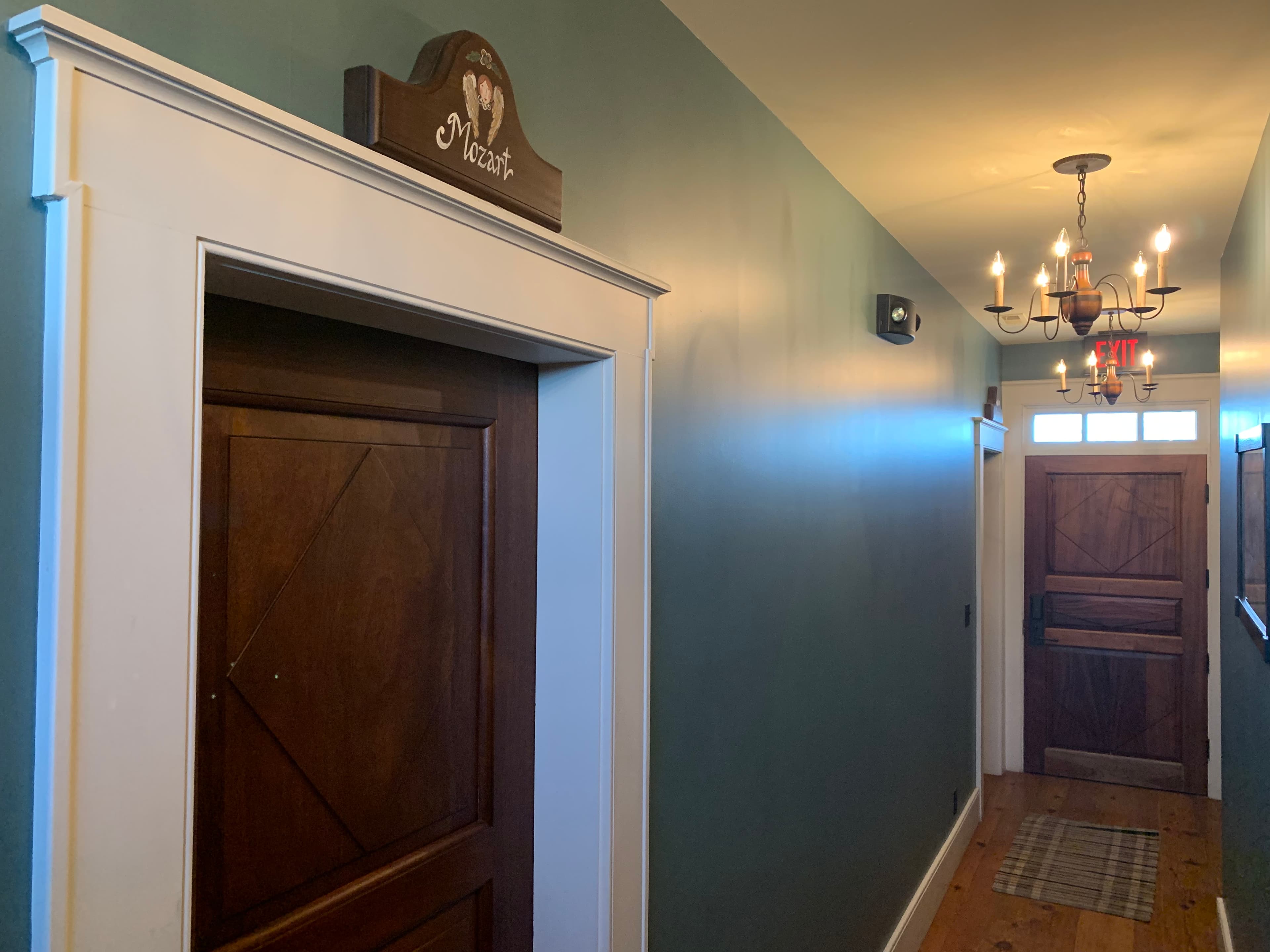A hallway with a wooden door labeled "Mozart" and a chandelier overhead.