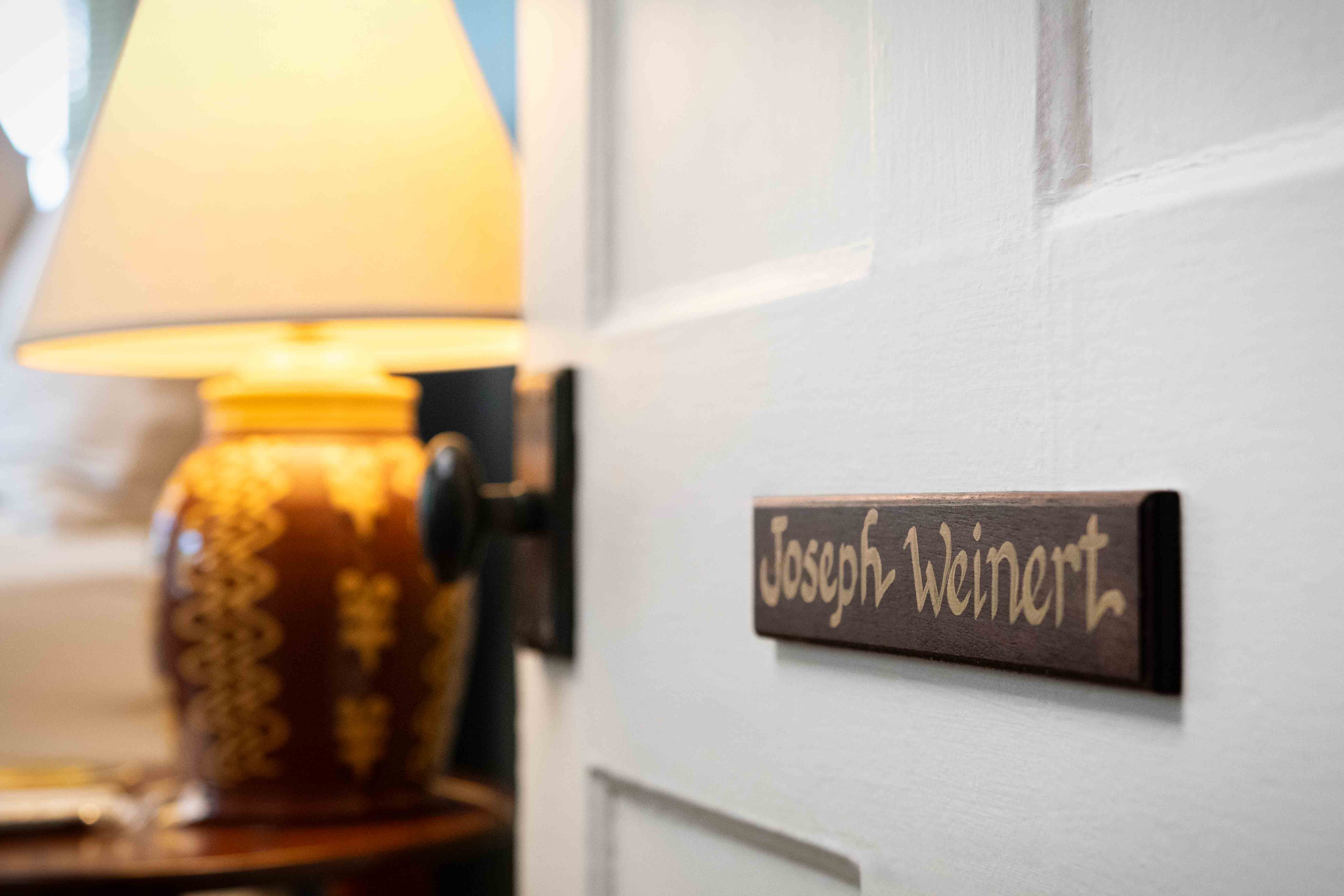 A door with a nameplate reading "Joseph Weinert" beside a lamp.