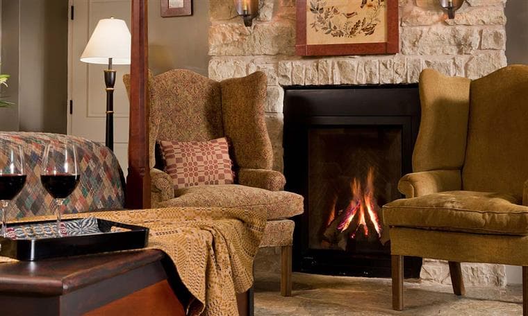 A cozy living room featuring two armchairs, a fireplace, and glasses of red wine on a table.