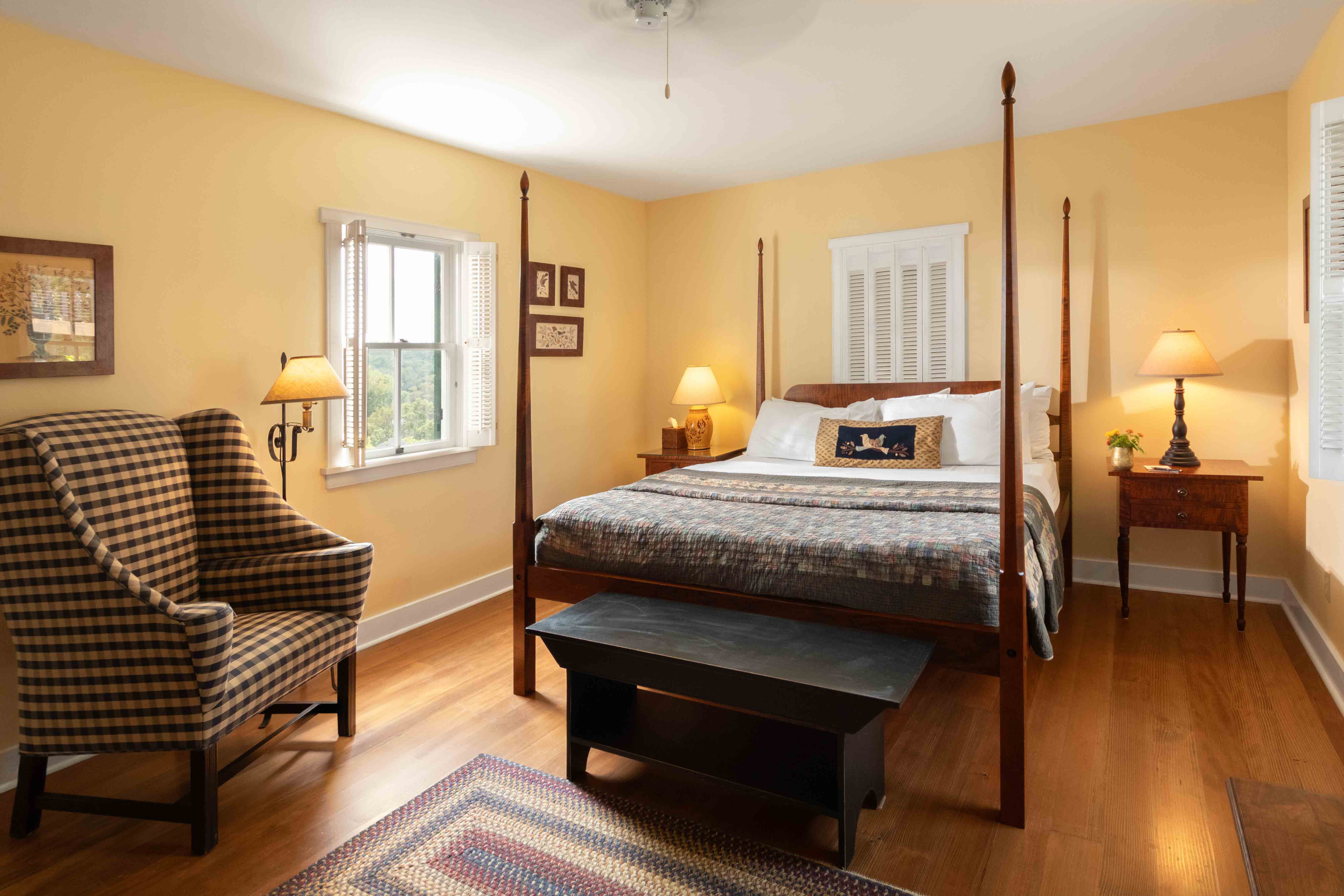 A cozy bedroom featuring a four-poster bed, a checkered armchair, and warm yellow walls.