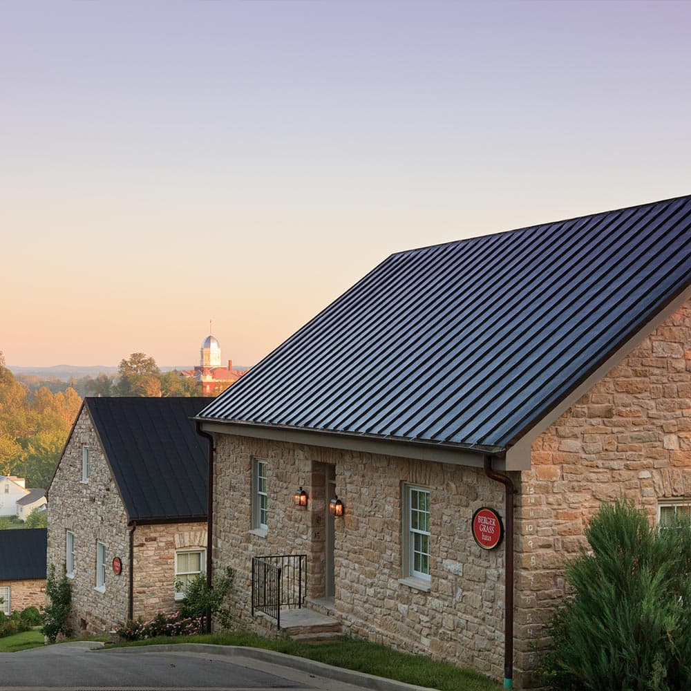 A stone house with a dark metal roof is framed against a pastel sky at sunset.