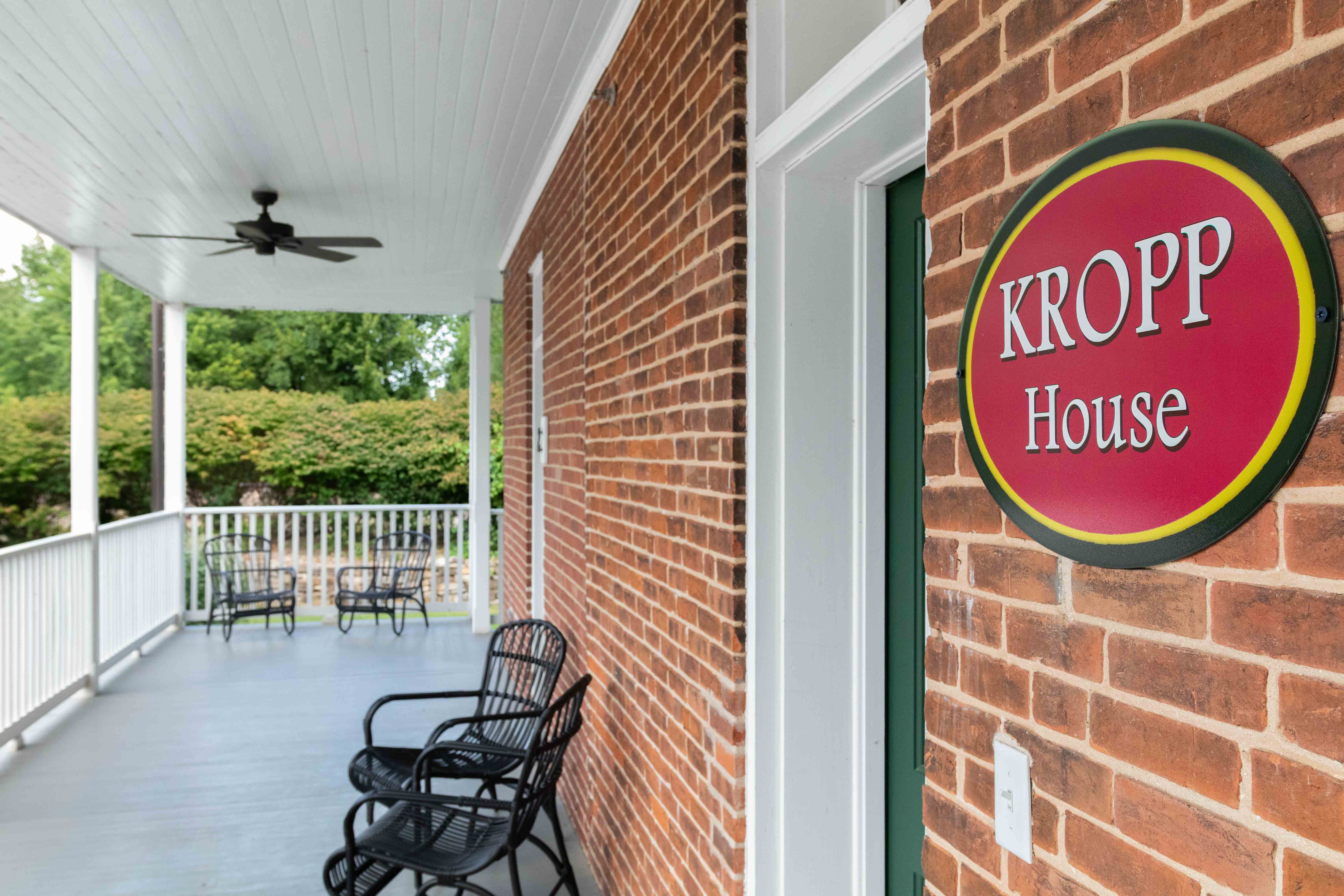 A brick wall features a sign reading "KROPP House," with a porch and chairs visible in the background.