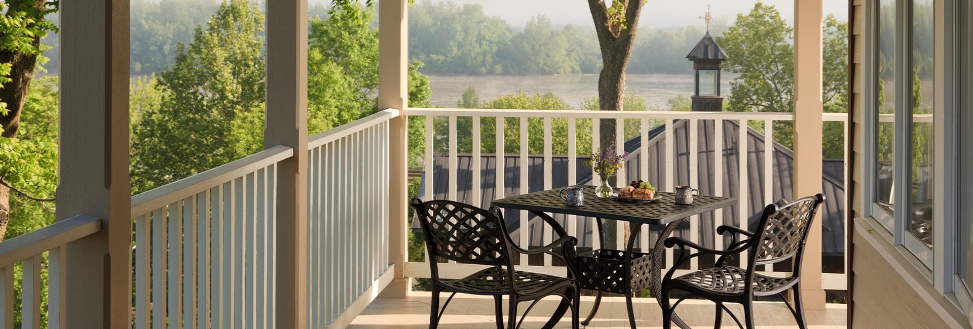 A serene balcony with a table set for breakfast overlooking a lush green landscape.