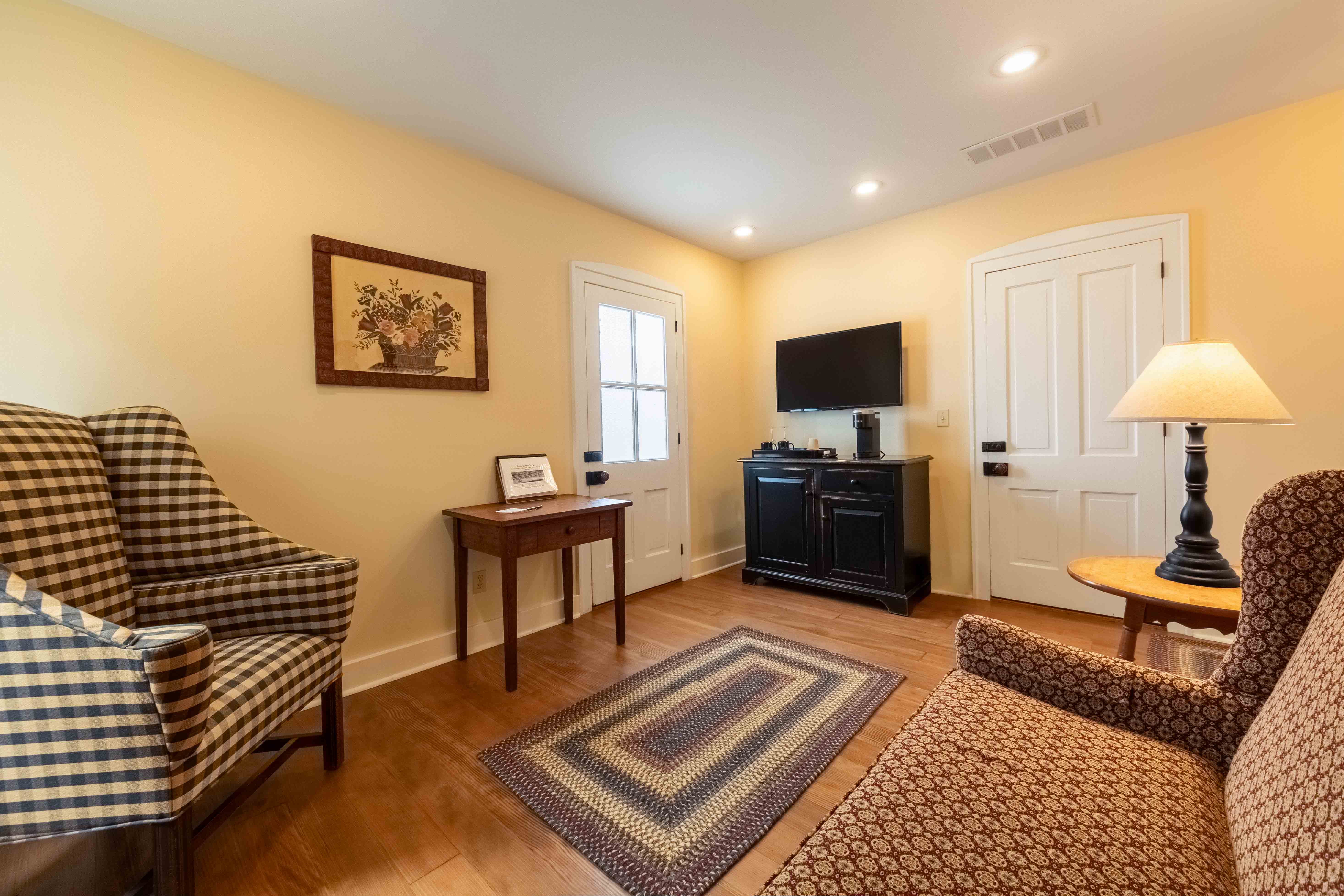 A cozy living room featuring two patterned chairs, a small table, a television, and a door leading outside.