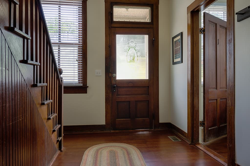 A cozy entrance hallway featuring a wooden door, stairway, and textured rug.