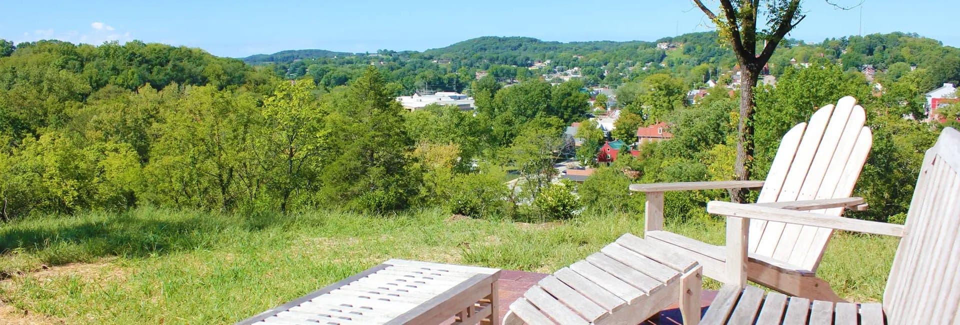 A scenic view of a green landscape with wooden chairs overlooking a small town.