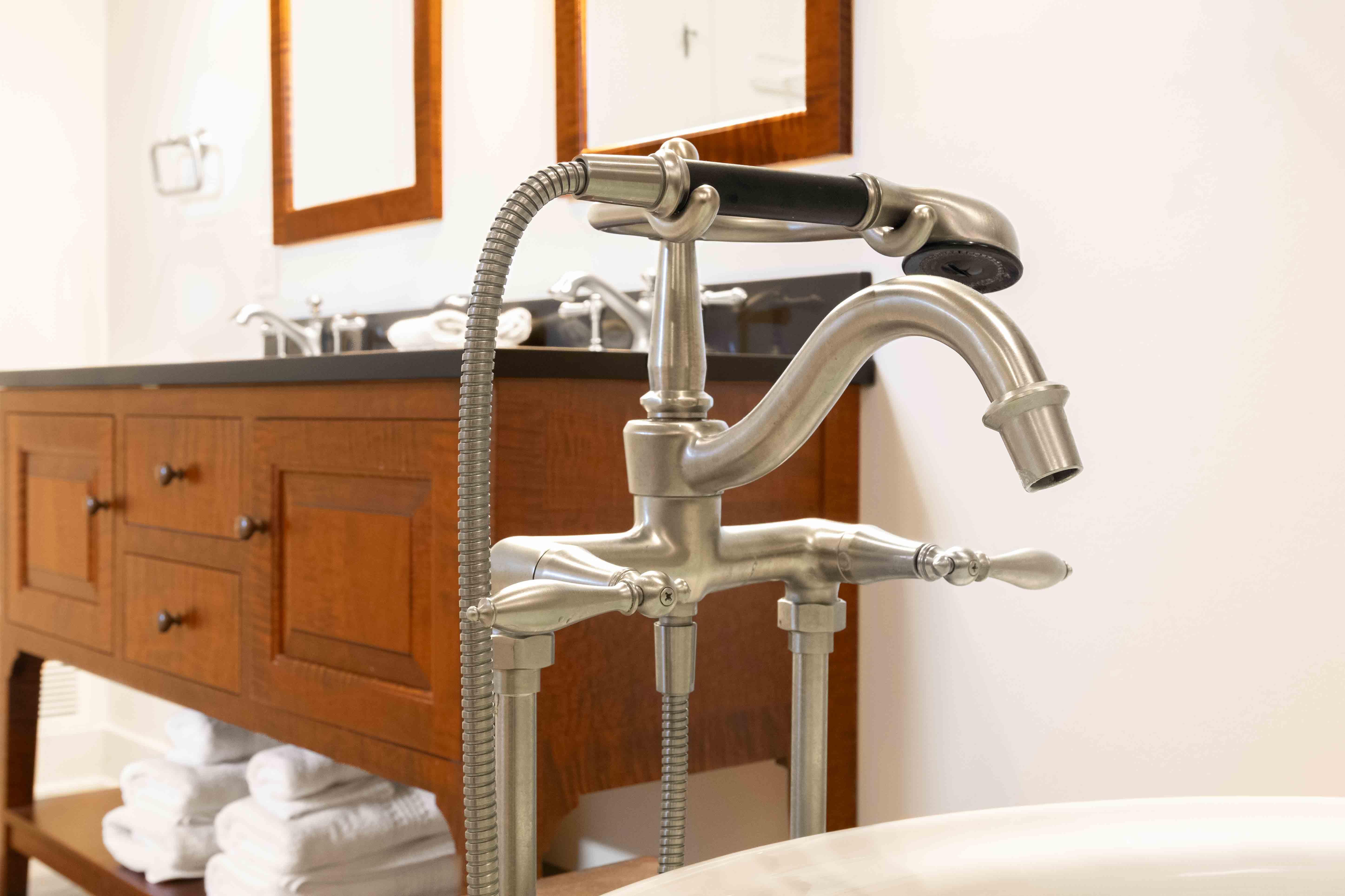 A vintage-style faucet with a black handle is positioned in front of a wooden vanity in a bright bathroom.