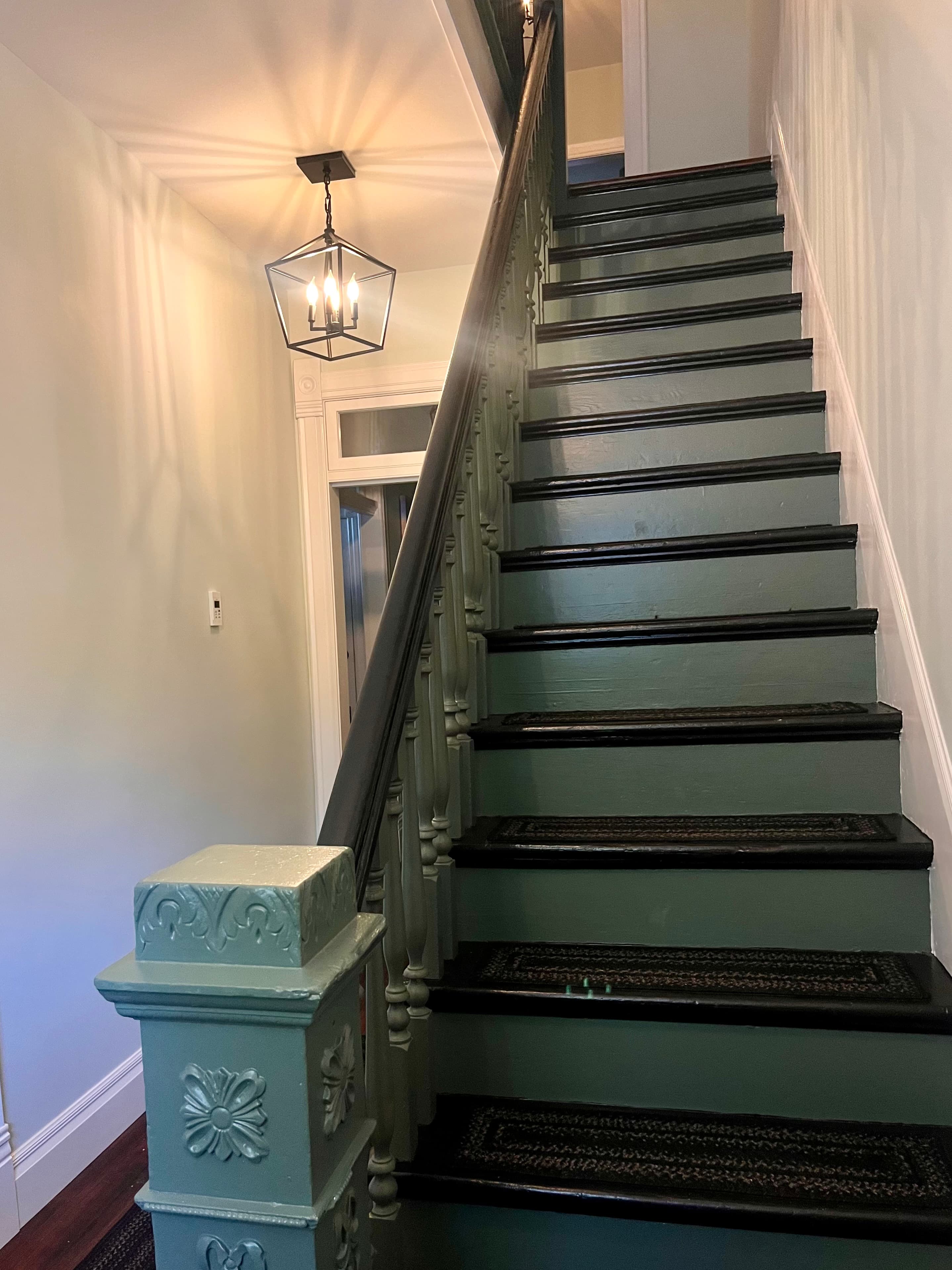 A view of a green staircase leading up, with a hanging light fixture above.