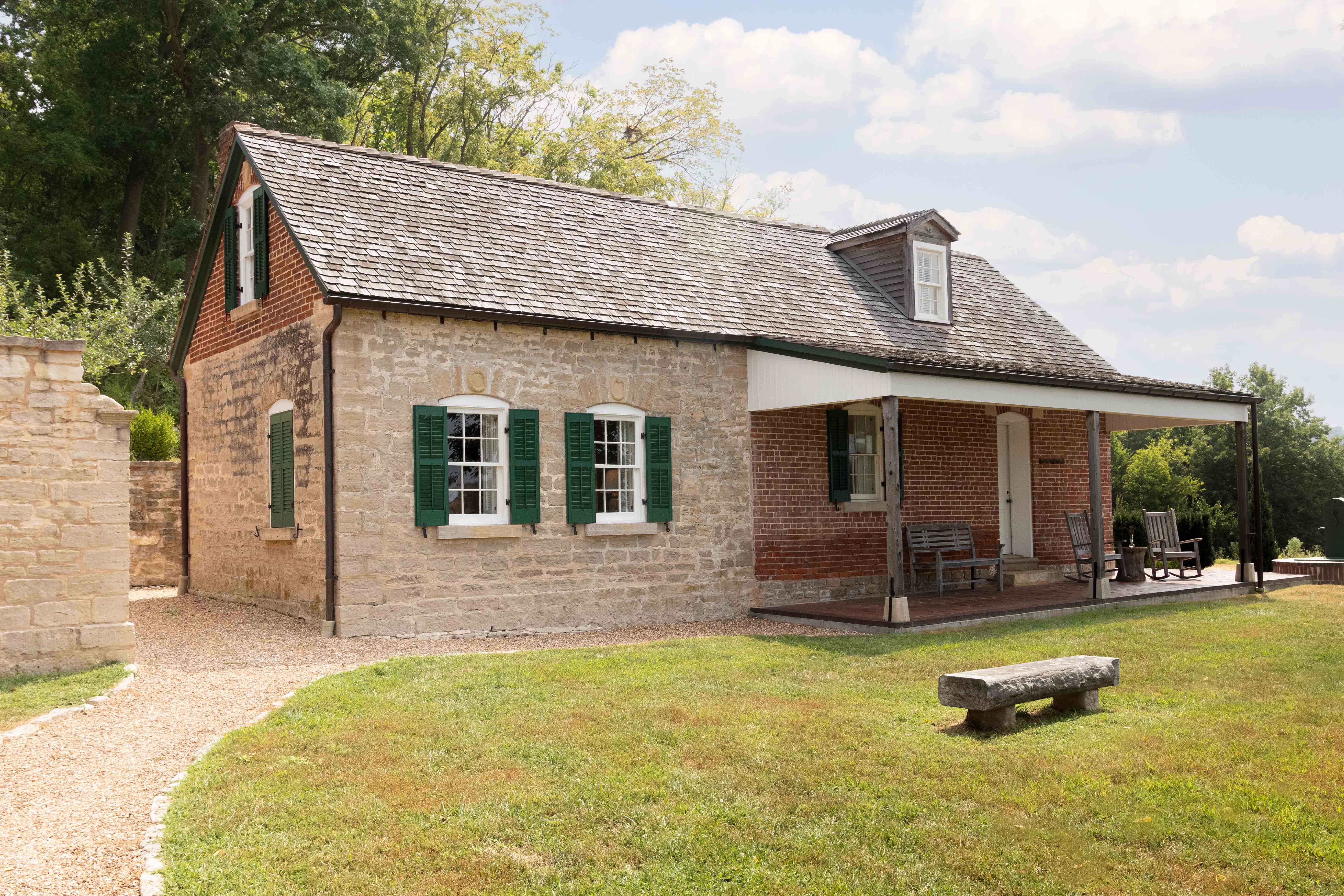 A charming two-story house featuring a mix of stone and brick, with green shutters and a covered porch.