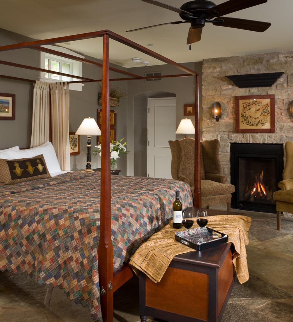 Cozy bedroom featuring a four-poster bed, stone fireplace, and a wine setup.