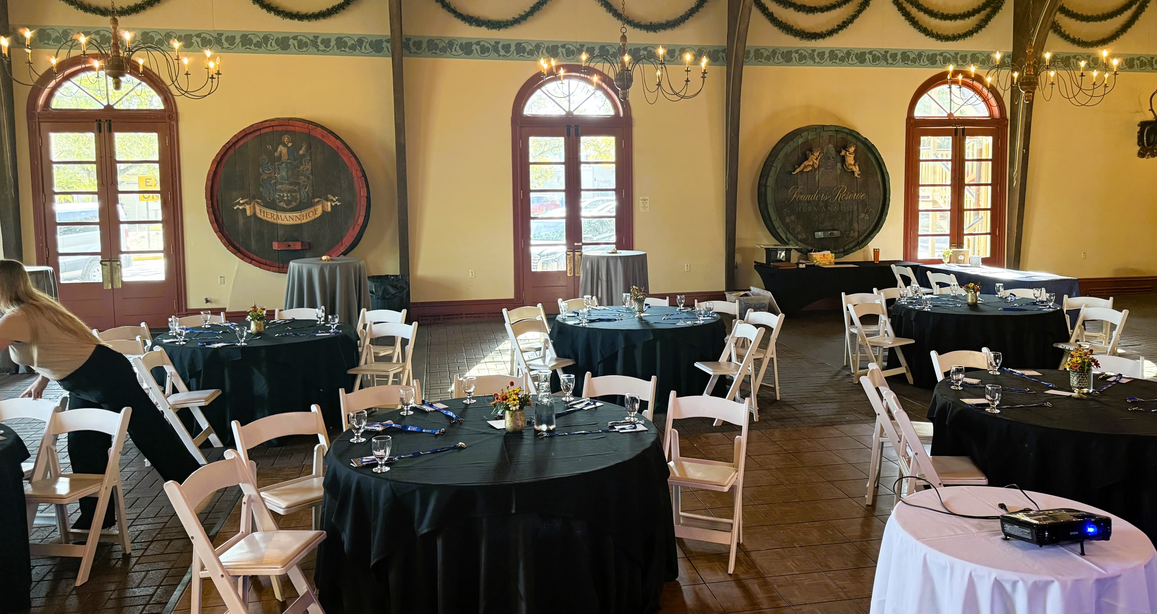 An elegantly decorated event space with round tables set for dining and large windows allowing natural light.