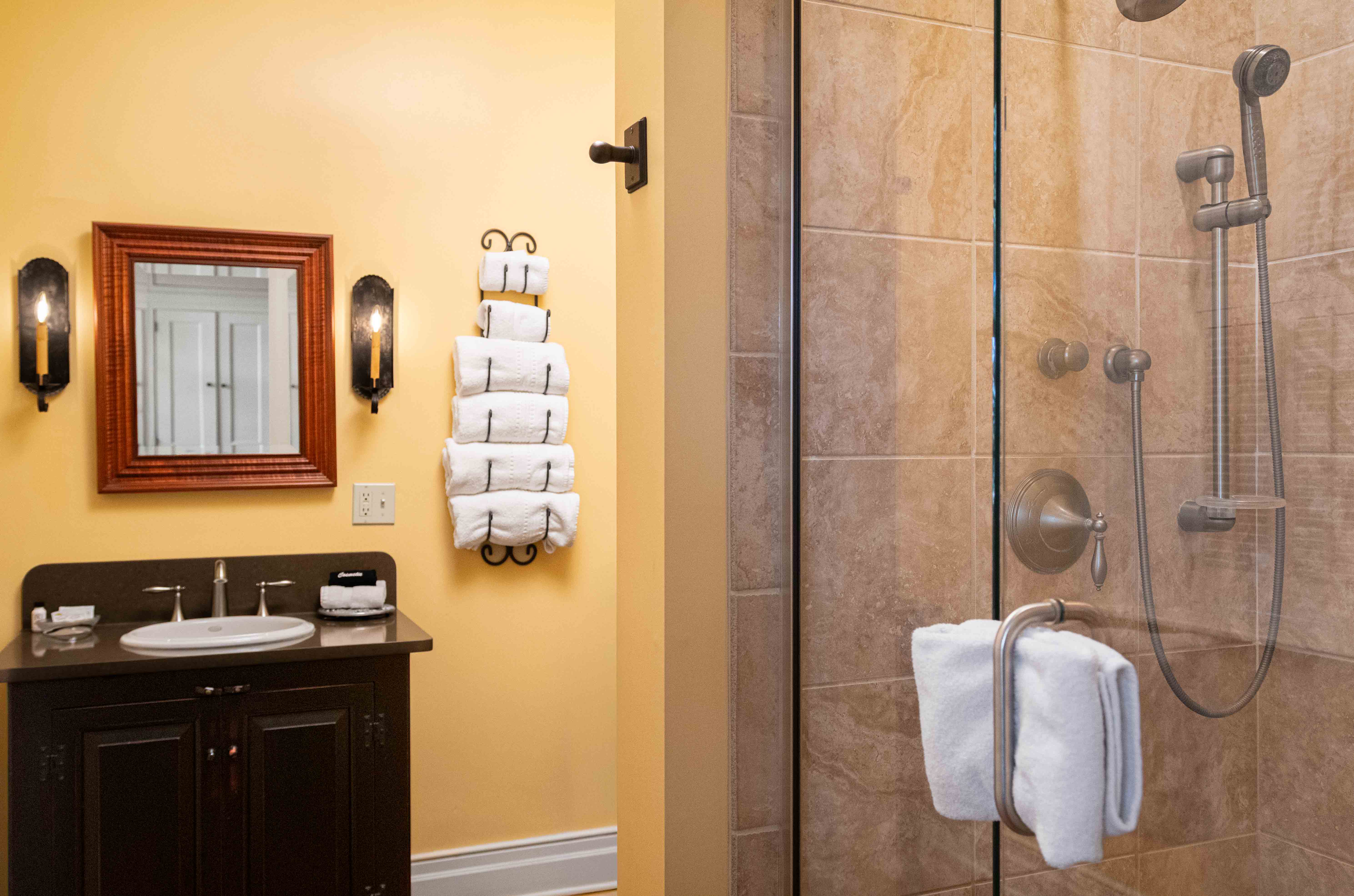 A modern bathroom featuring a shower, sink, and neatly arranged towels on a wall rack against a yellow background.