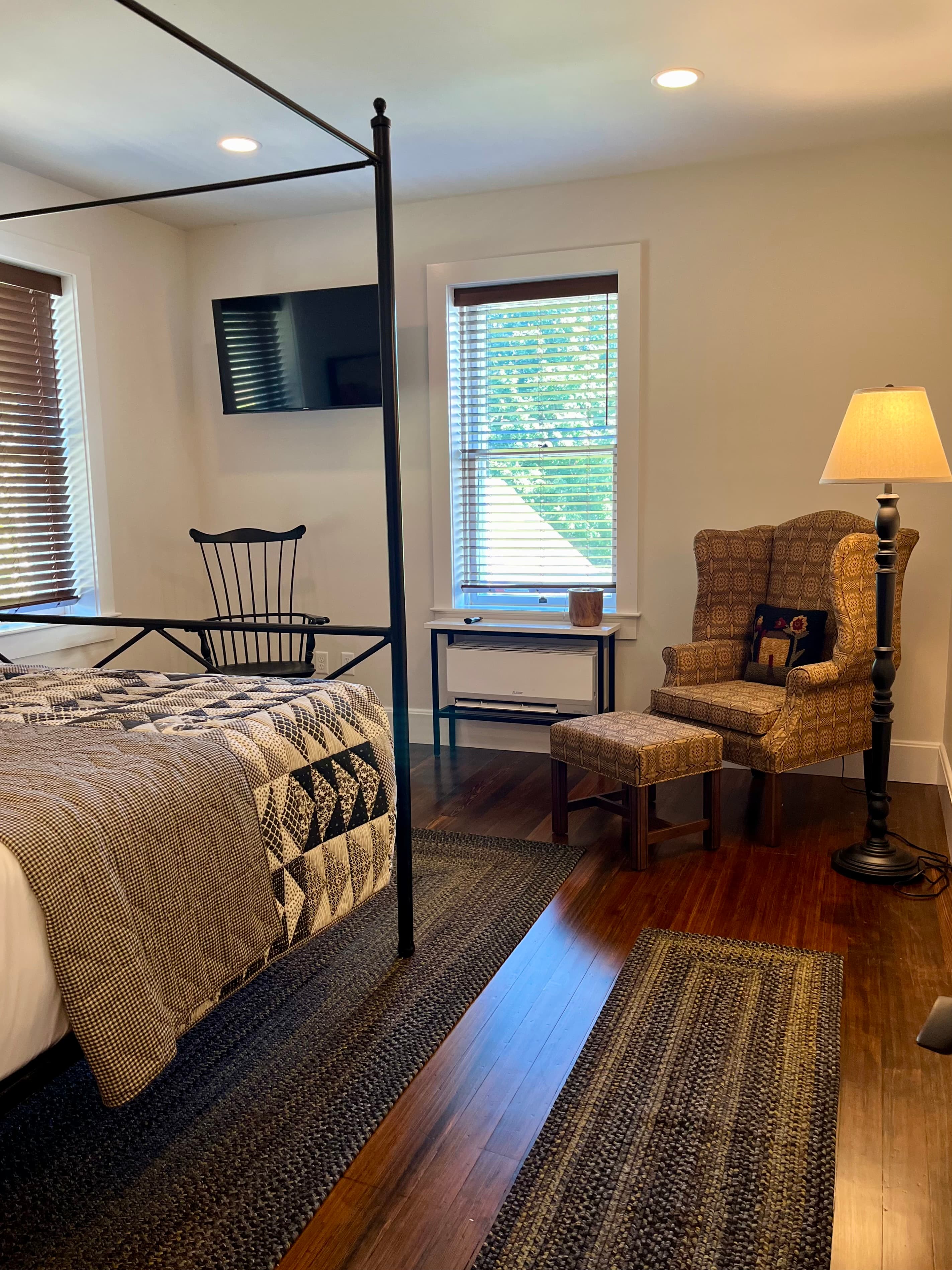 A cozy bedroom featuring a four-poster bed, armchair, and a flat-screen TV on the wall.