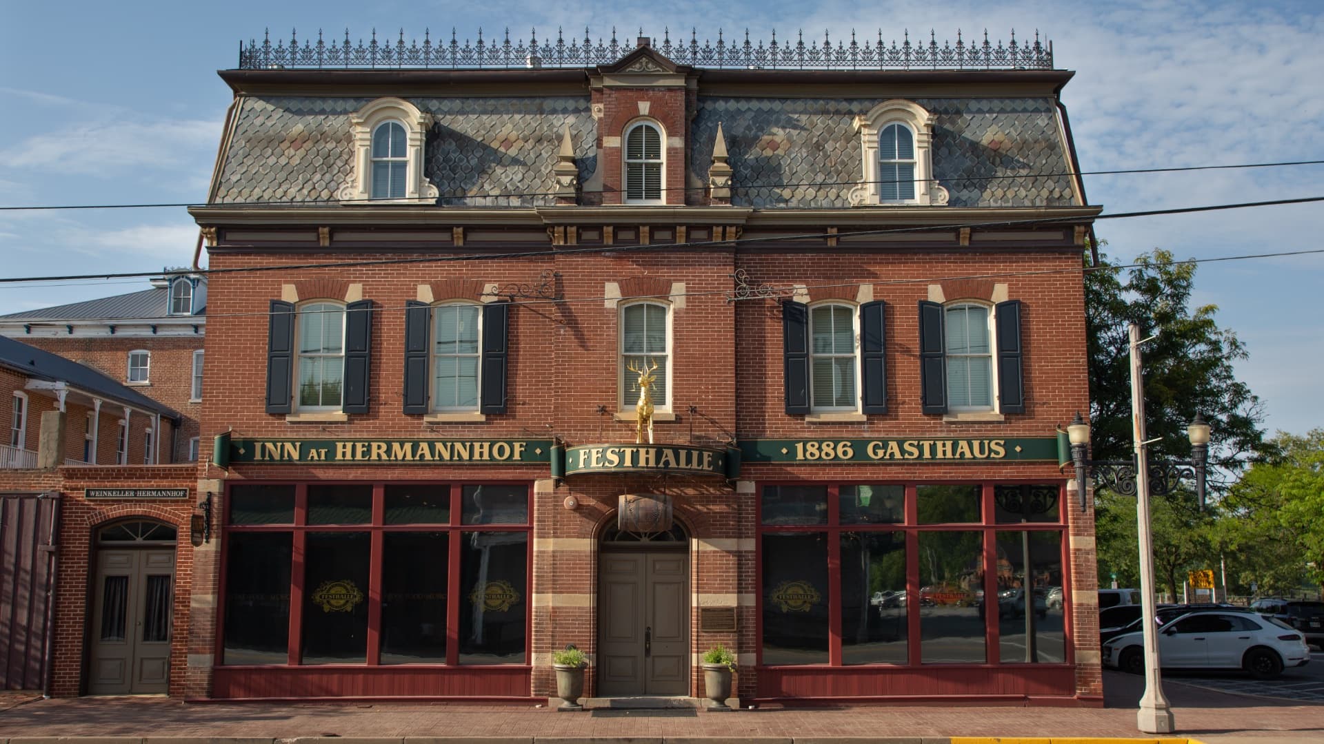 A brick building featuring a sloped roof and a golden stag statue above the entrance, labeled "Inn at Hermannhof".