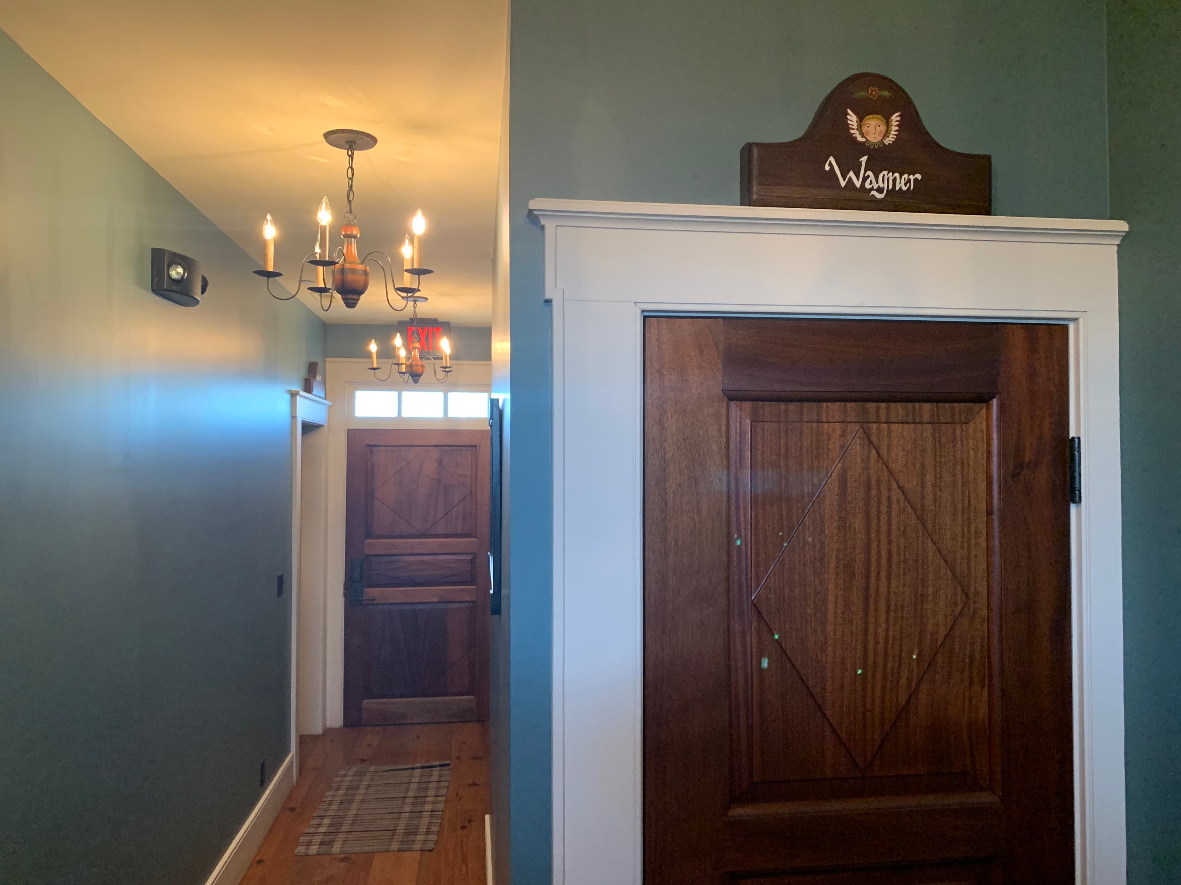 A hallway with a wooden door labeled "Wagner" and a chandelier above.