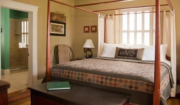 Cozy bedroom featuring a four-poster bed, decorative quilt, and an adjacent bathroom.