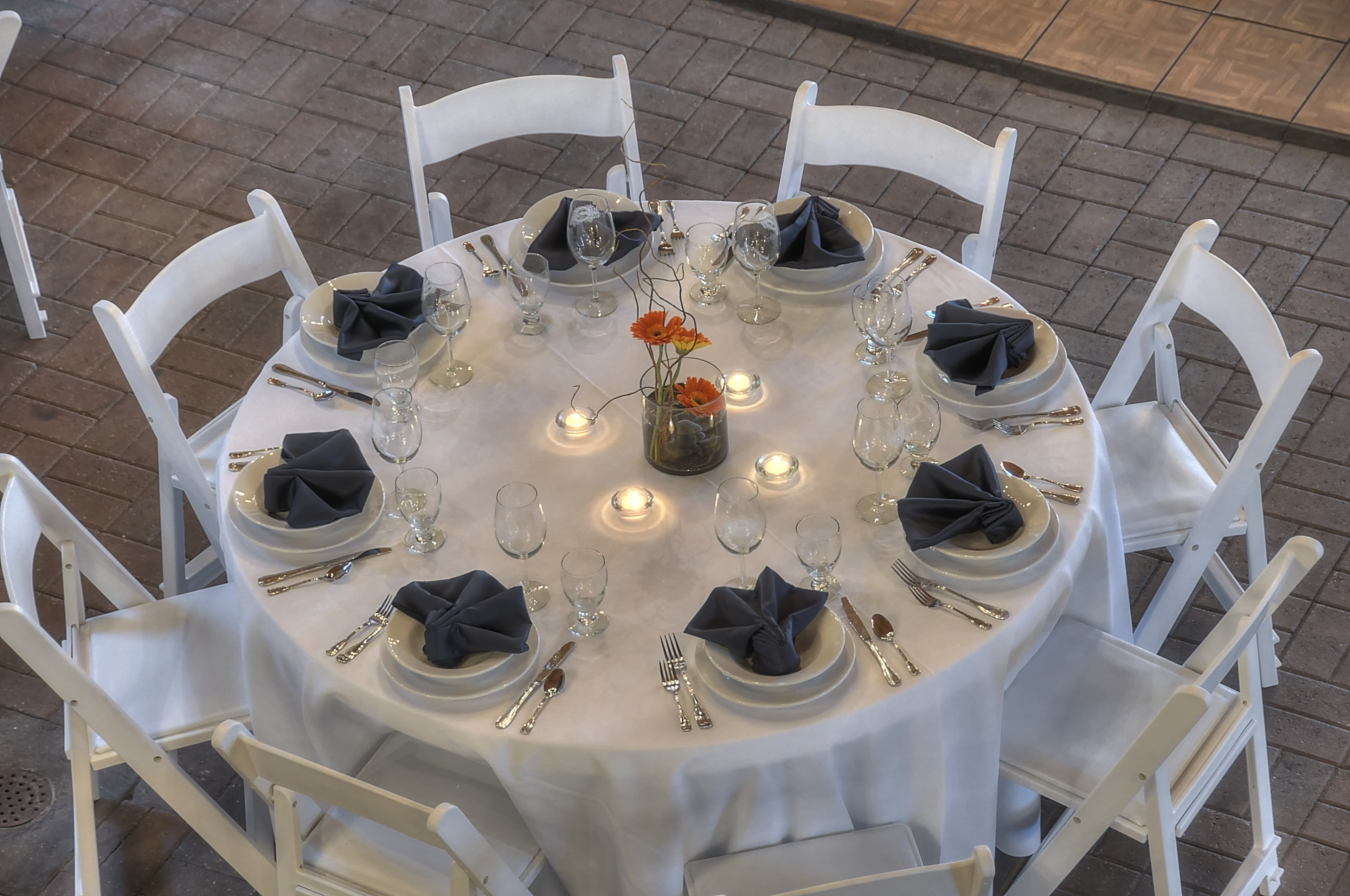 A round dining table elegantly set with black napkins, glassware, and a floral centerpiece.