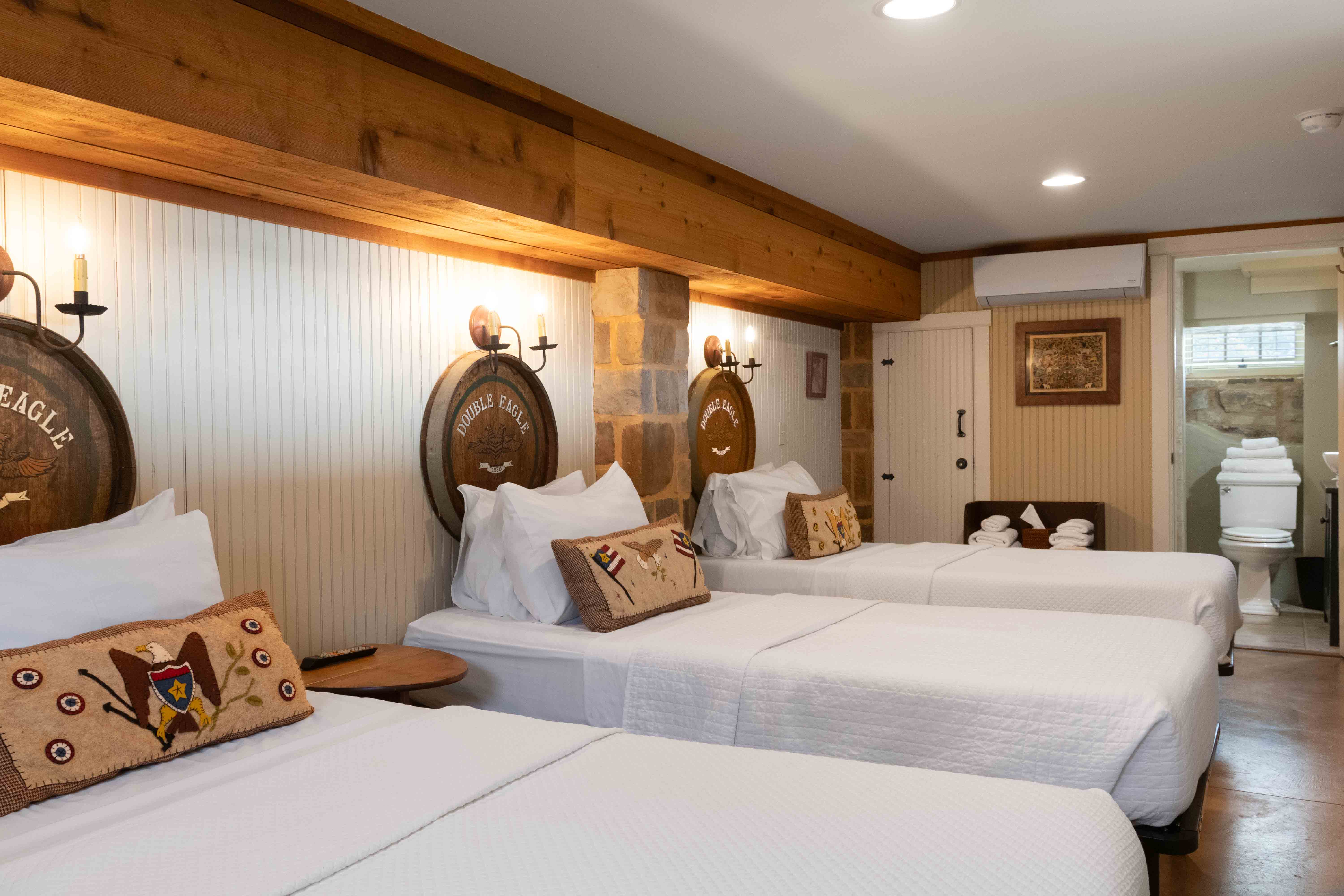 A cozy guest room featuring three neatly made beds with rustic decor and wooden accents.