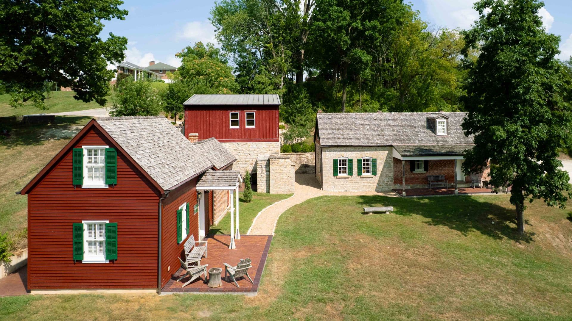 Aerial view of two rustic houses with green shutters and a path leading through a grassy area.