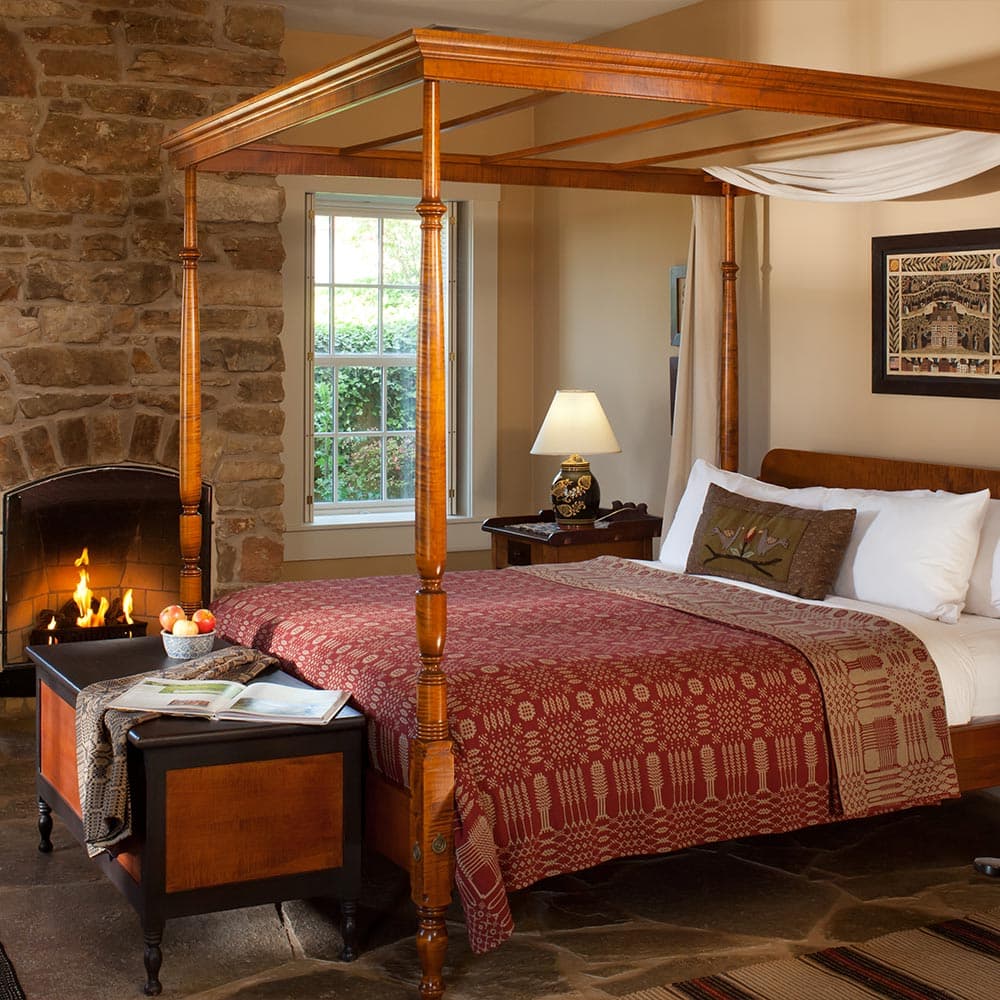 A cozy bedroom featuring a four-poster bed, stone fireplace, and warm lighting.