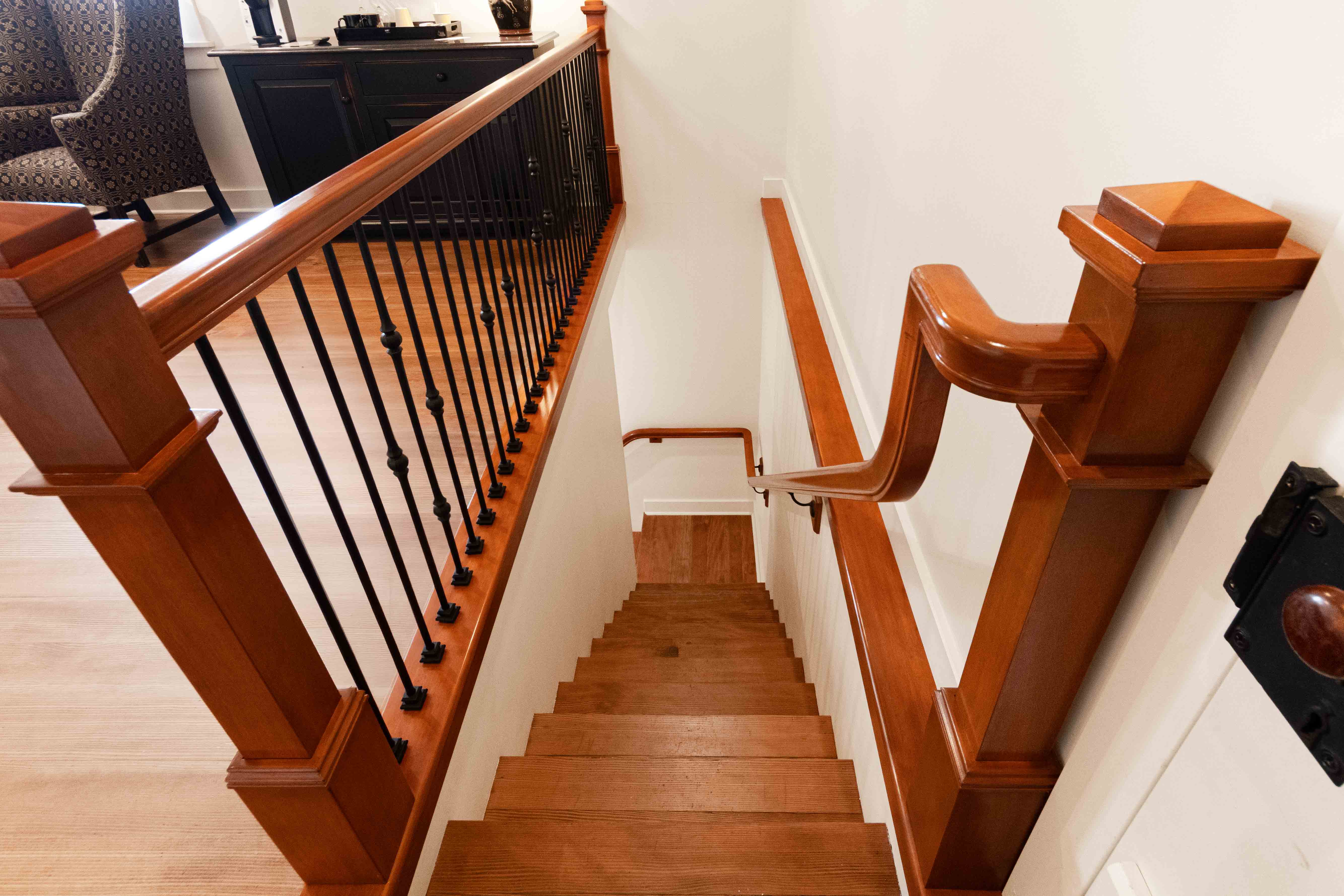 Wooden staircase leading down with polished railing and black iron balusters.