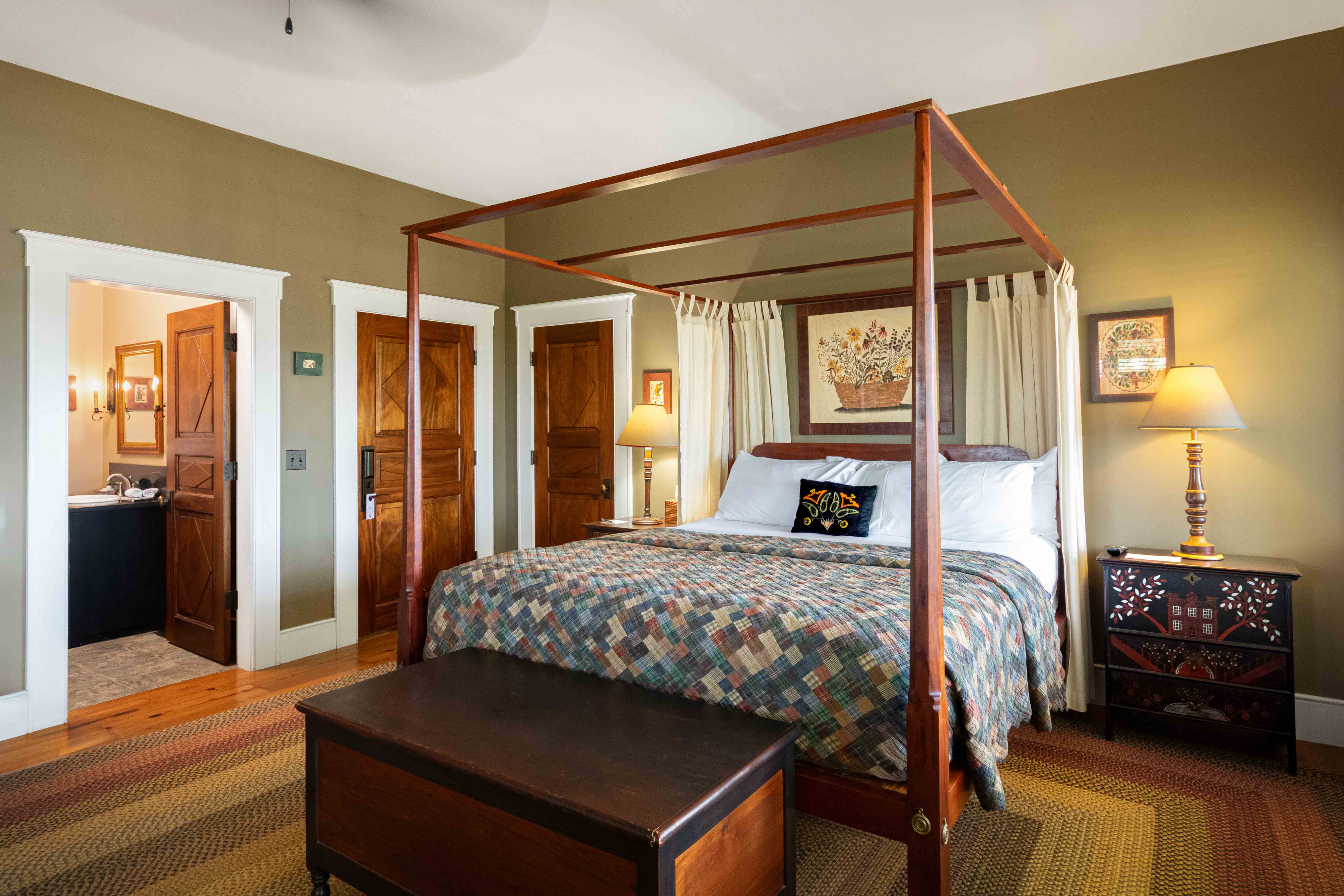 Cozy bedroom featuring a four-poster bed, decorative quilt, and warm lighting with adjacent doors leading to a bathroom.