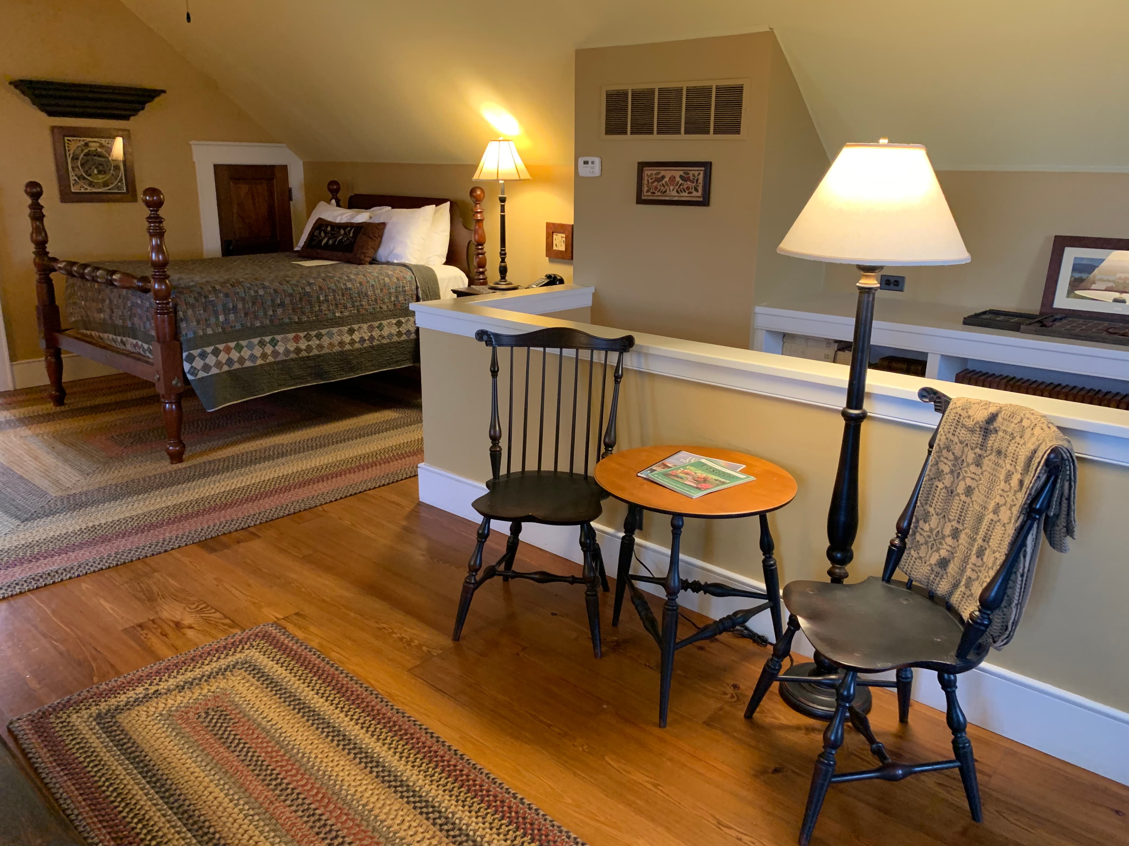 A cozy bedroom featuring a four-poster bed, two wooden chairs, and a small table with a book.