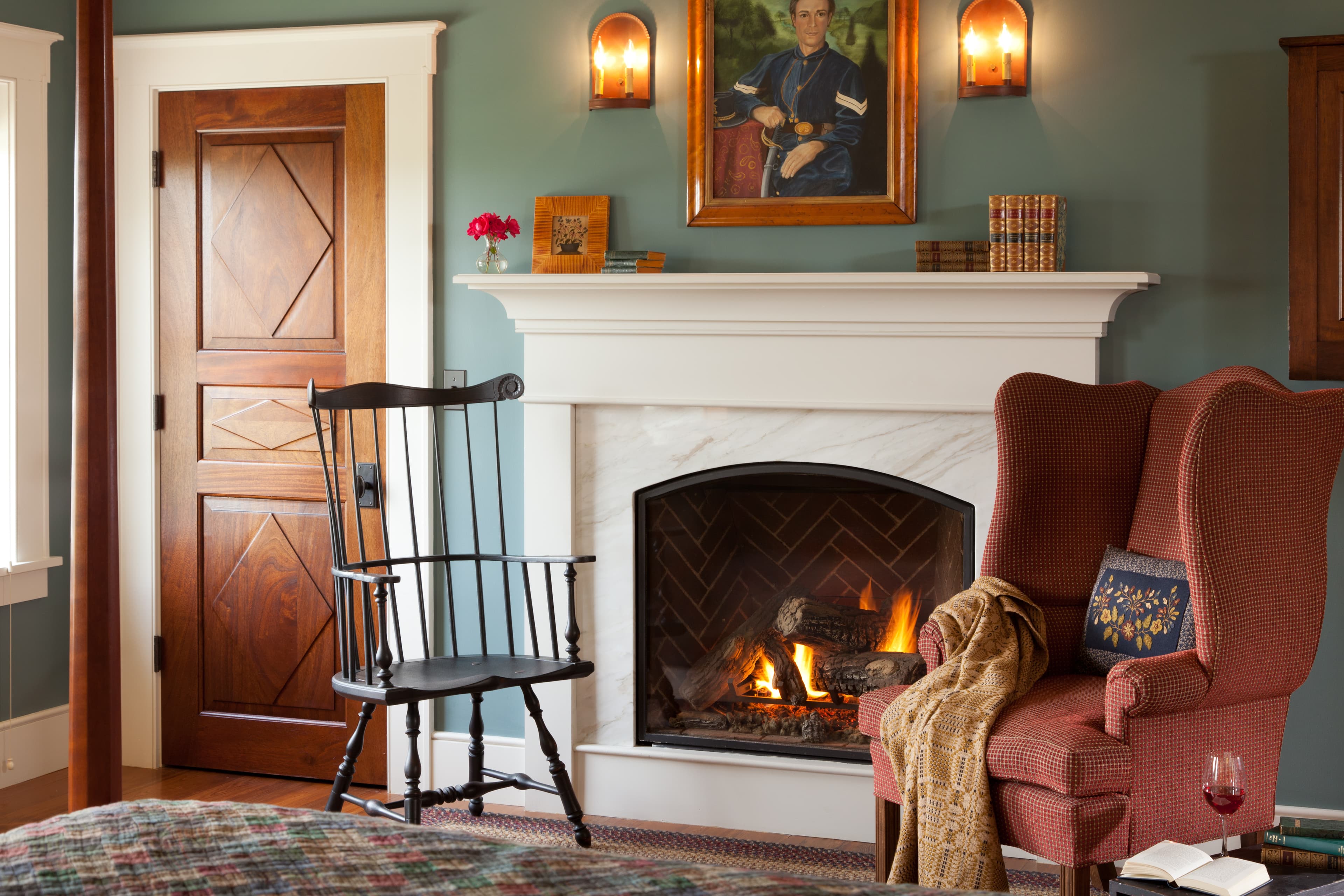 A cozy living space featuring a fireplace, two armchairs, a decorative portrait, and a wooden door.