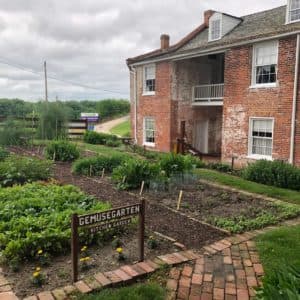 A brick house next to a garden with vegetables and a sign reading "Gemüse Garten."