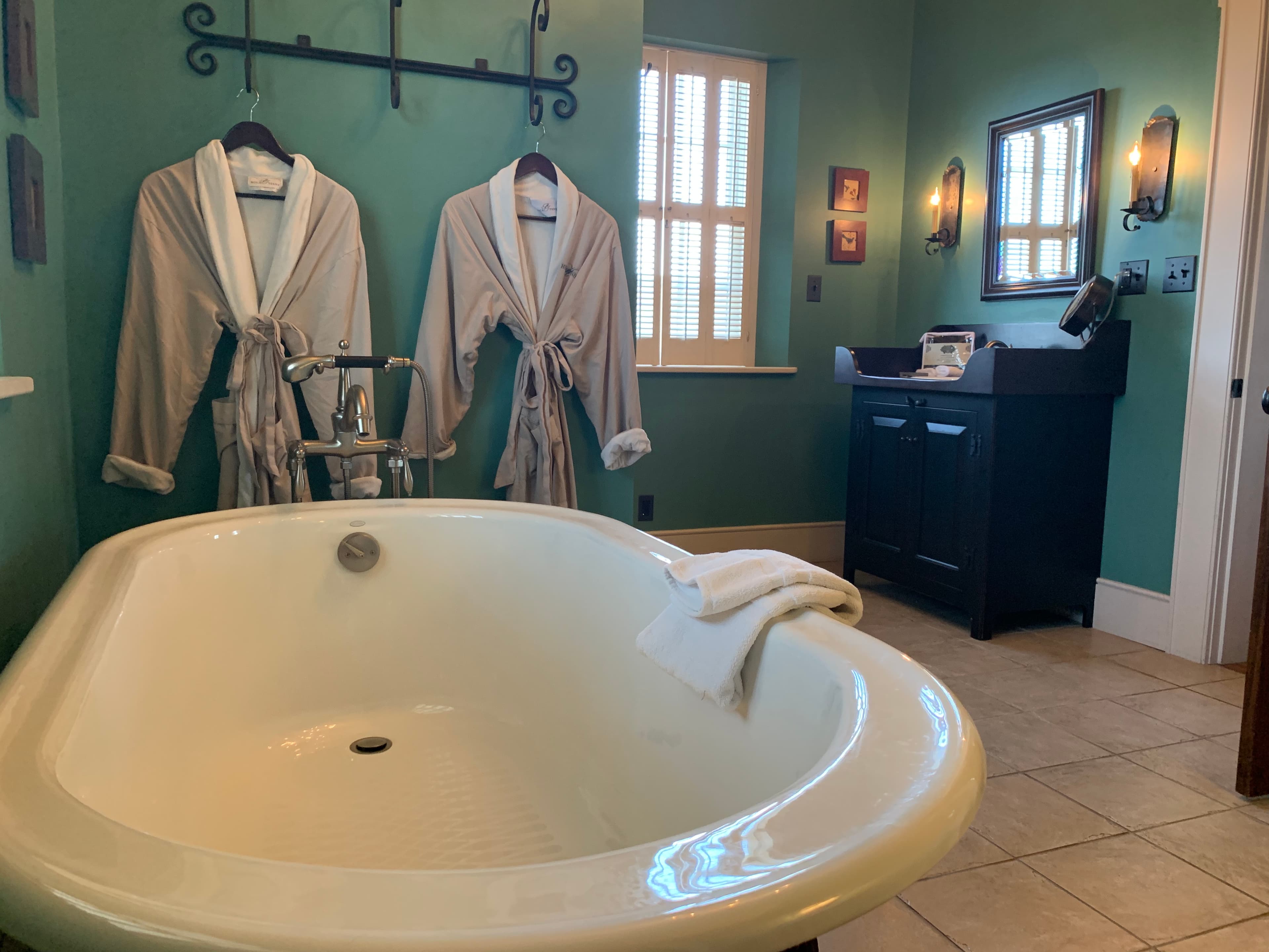 A cozy bathroom featuring a freestanding tub, two hanging robes, and a dark wood vanity.