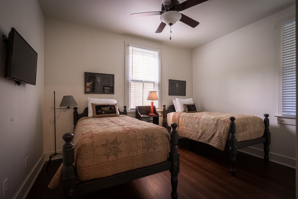 A cozy bedroom with two twin beds, a ceiling fan, and natural light from windows.