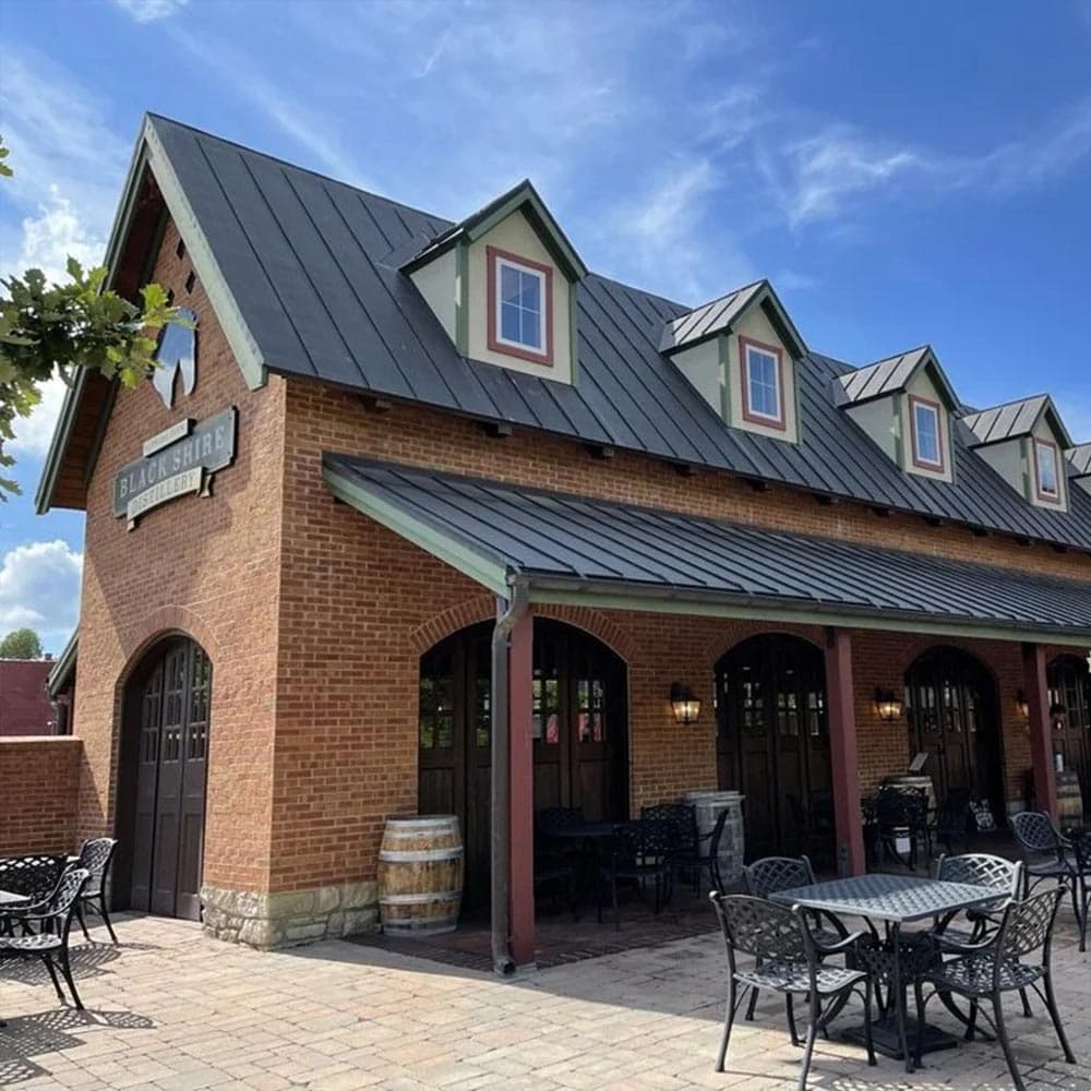 A brick building with a steep roof and outdoor seating area under a blue sky.
