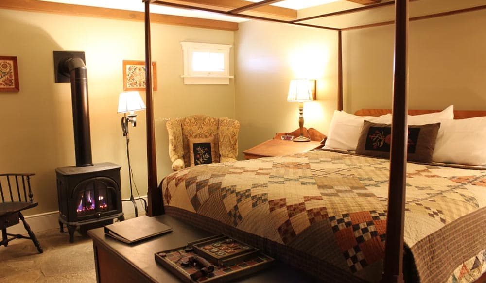 Cozy bedroom with a four-poster bed, quilts, and a wood stove.