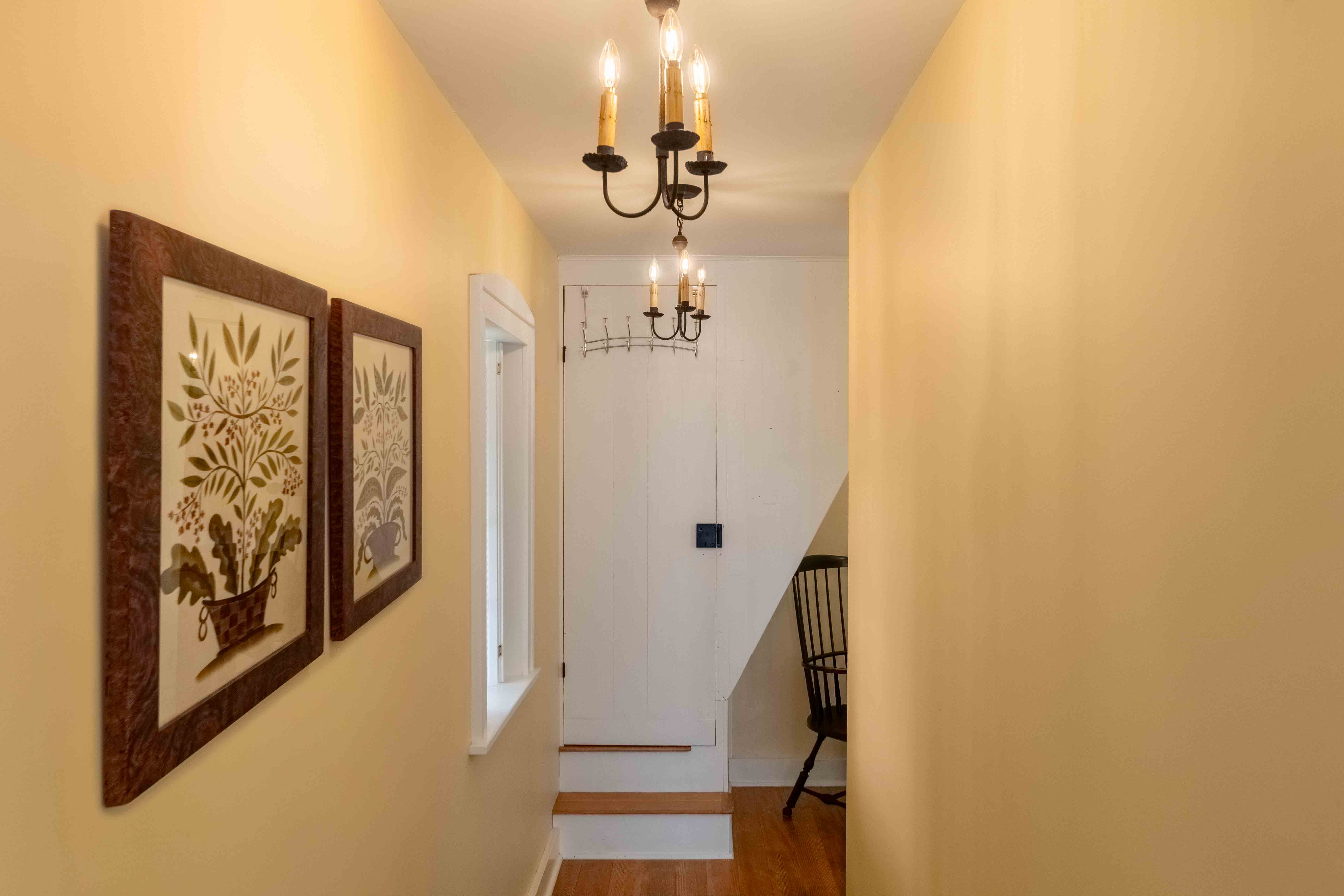A well-lit hallway featuring decorative wall art, a coat rack, and a chair against a yellow backdrop.