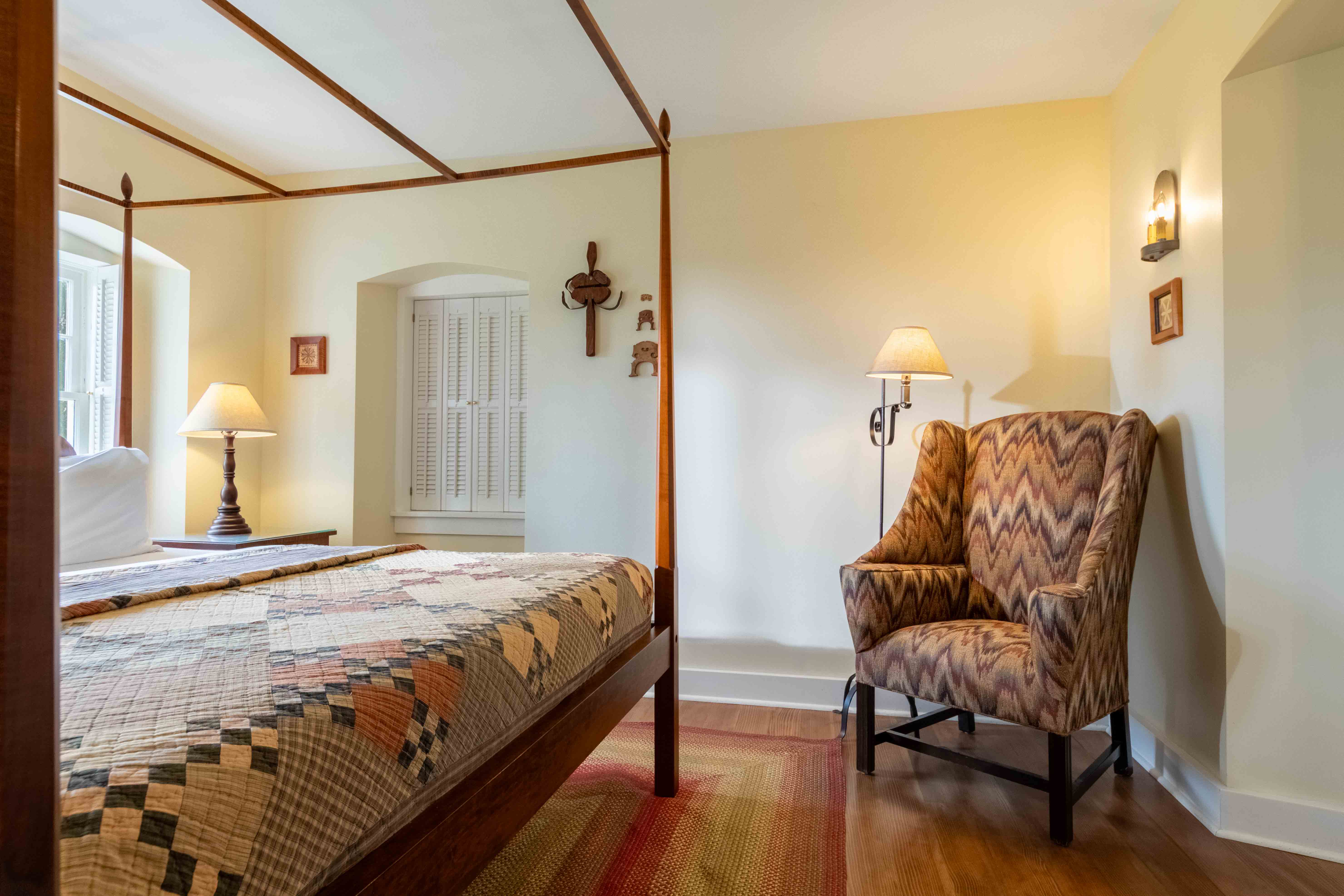 A cozy bedroom featuring a four-poster bed, a patterned armchair, and warm lighting.