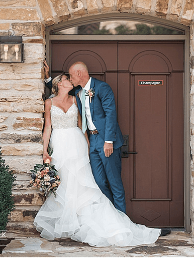 A bride and groom share a kiss in front of a rustic door, surrounded by natural stone.